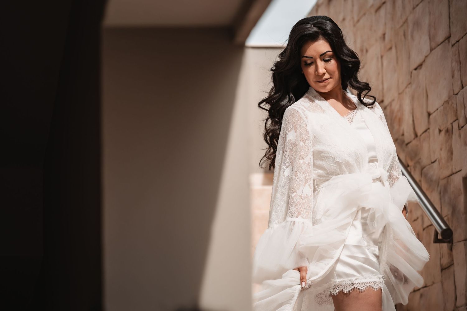 Dramatic side view of a flowing white lace wedding robe against a stone wall backdrop.
