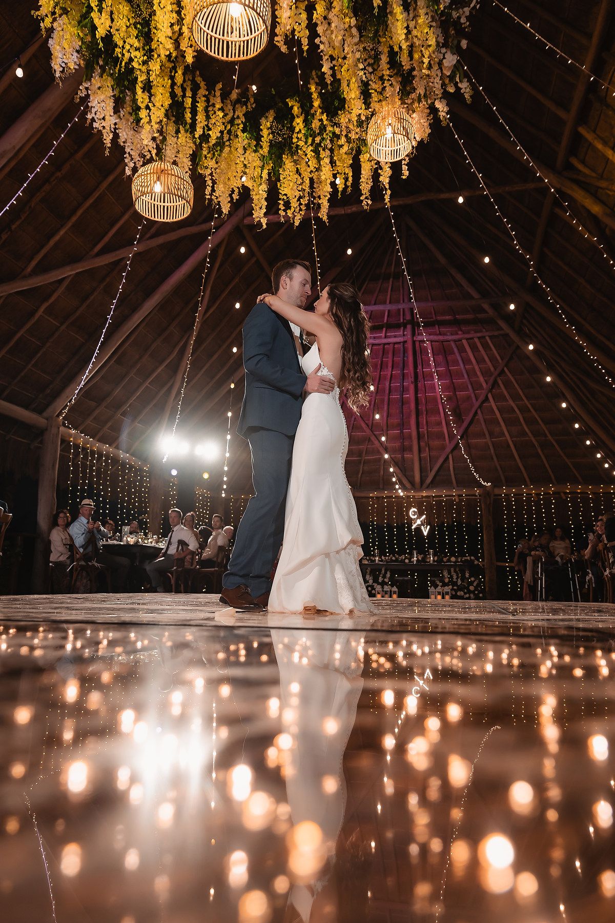 Romantic dance floor moment under glowing yellow floral installations and string lights.