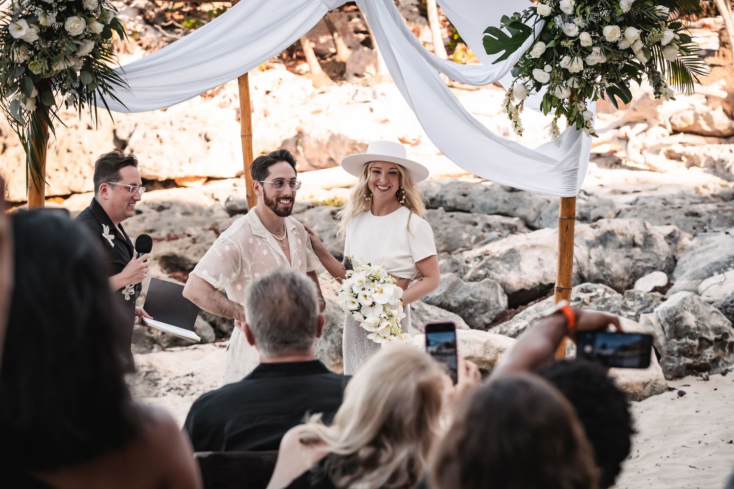 Outdoor wedding ceremony setup with white drapes and floral arrangements on rocky terrain.