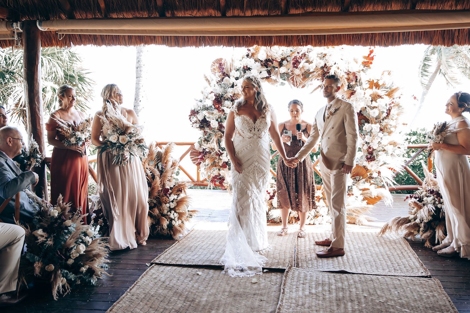 Wedding guests gather in a rustic covered outdoor venue with natural lighting and wooden beams.
