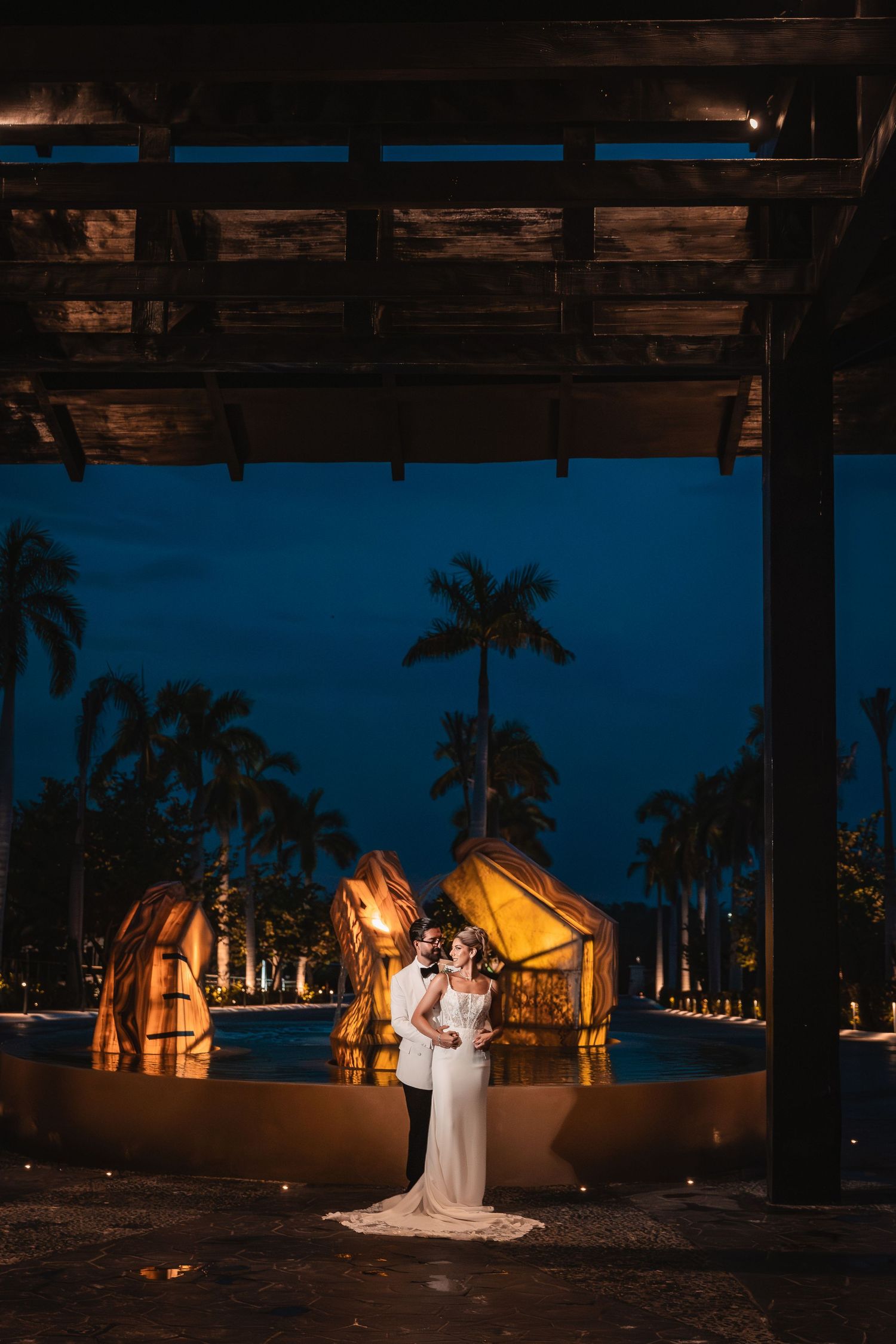 A romantic evening wedding ceremony under palm trees with glowing tent structures creating a magical ambiance.