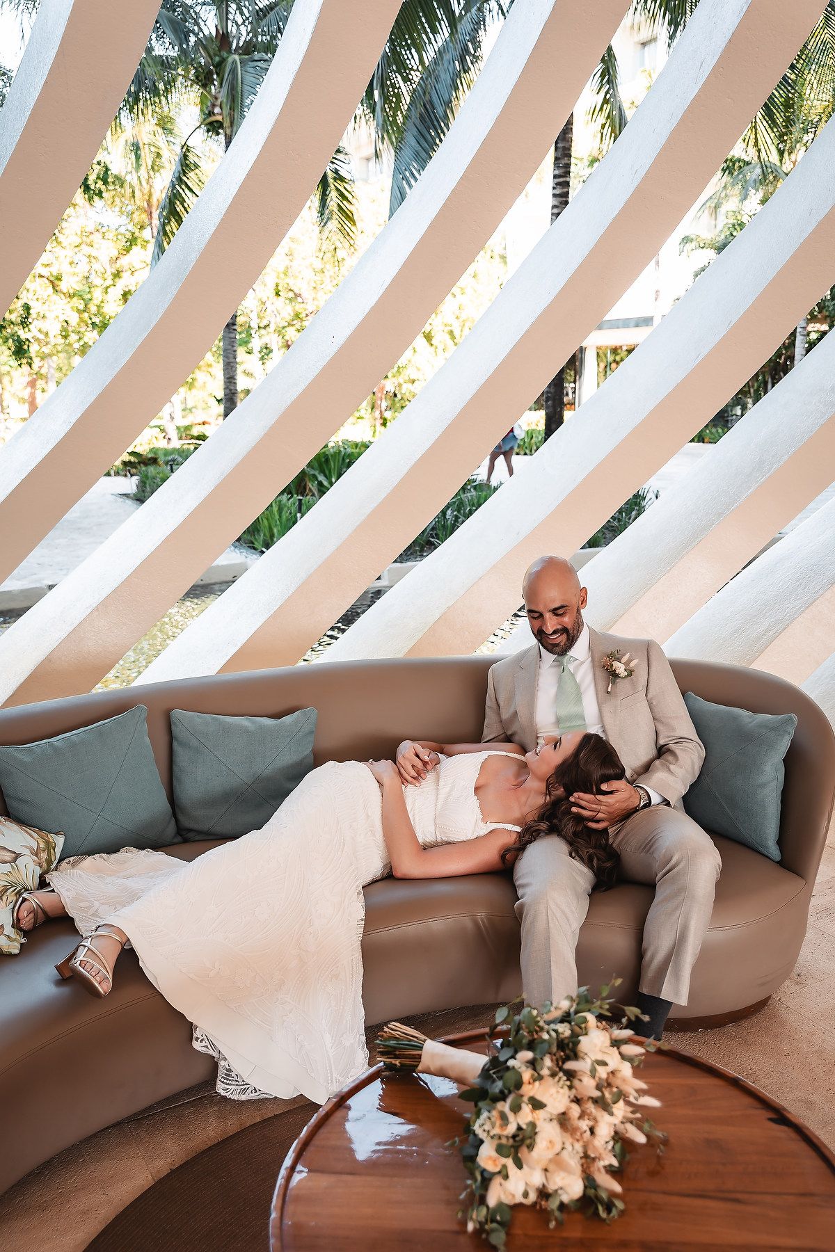 A couple relaxes on a beige couch under an architectural dome with tropical views.