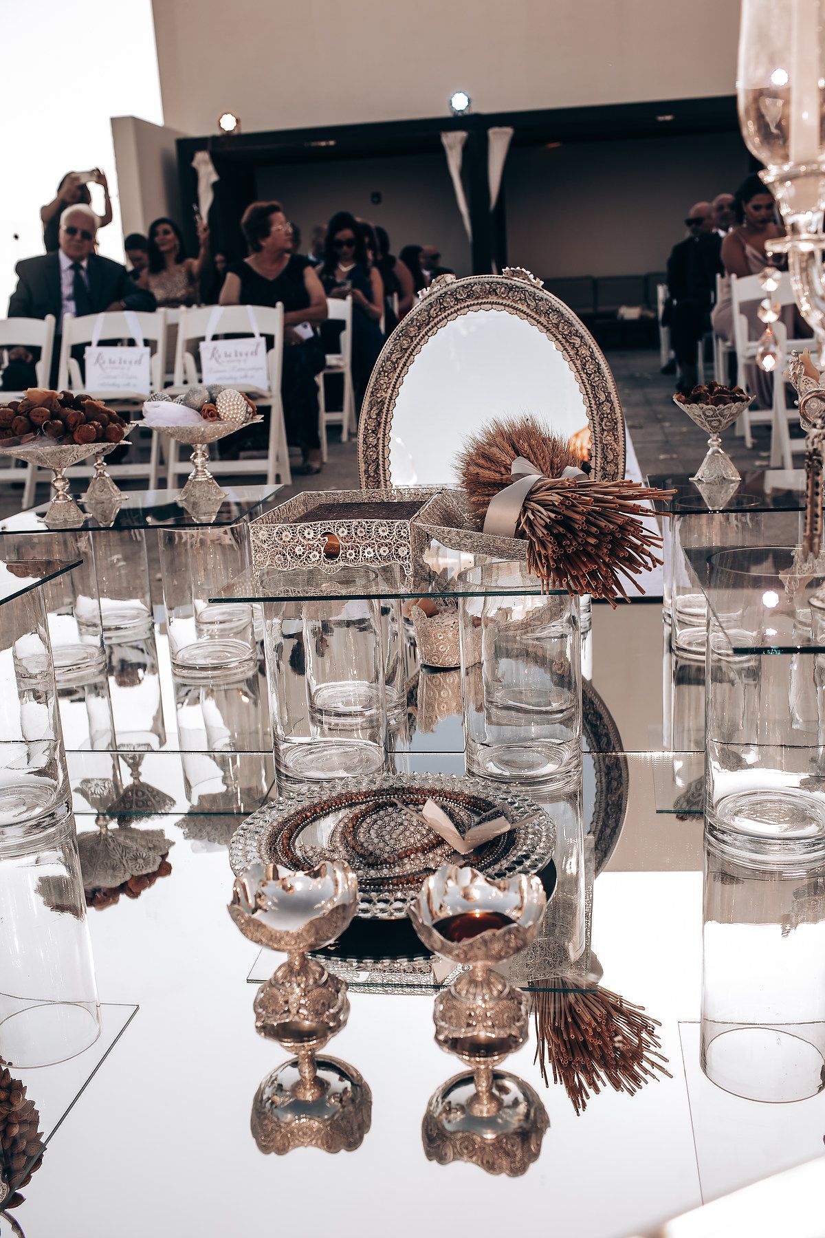 Elegant table setting with glass vessels and natural decorations displayed on a reflective mirrored surface.