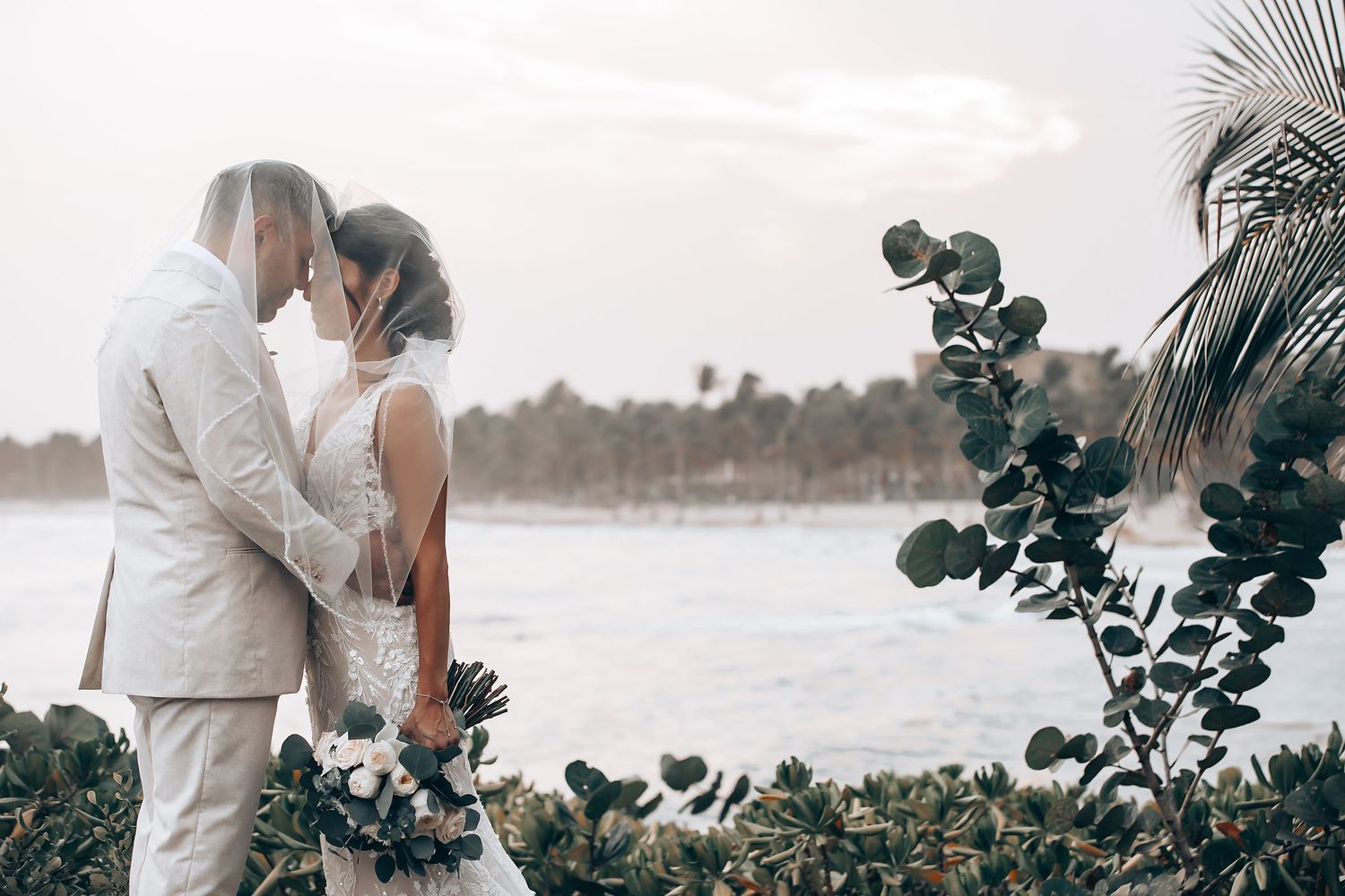 Romantic beachside wedding moments captured among swaying palm trees and tropical foliage.