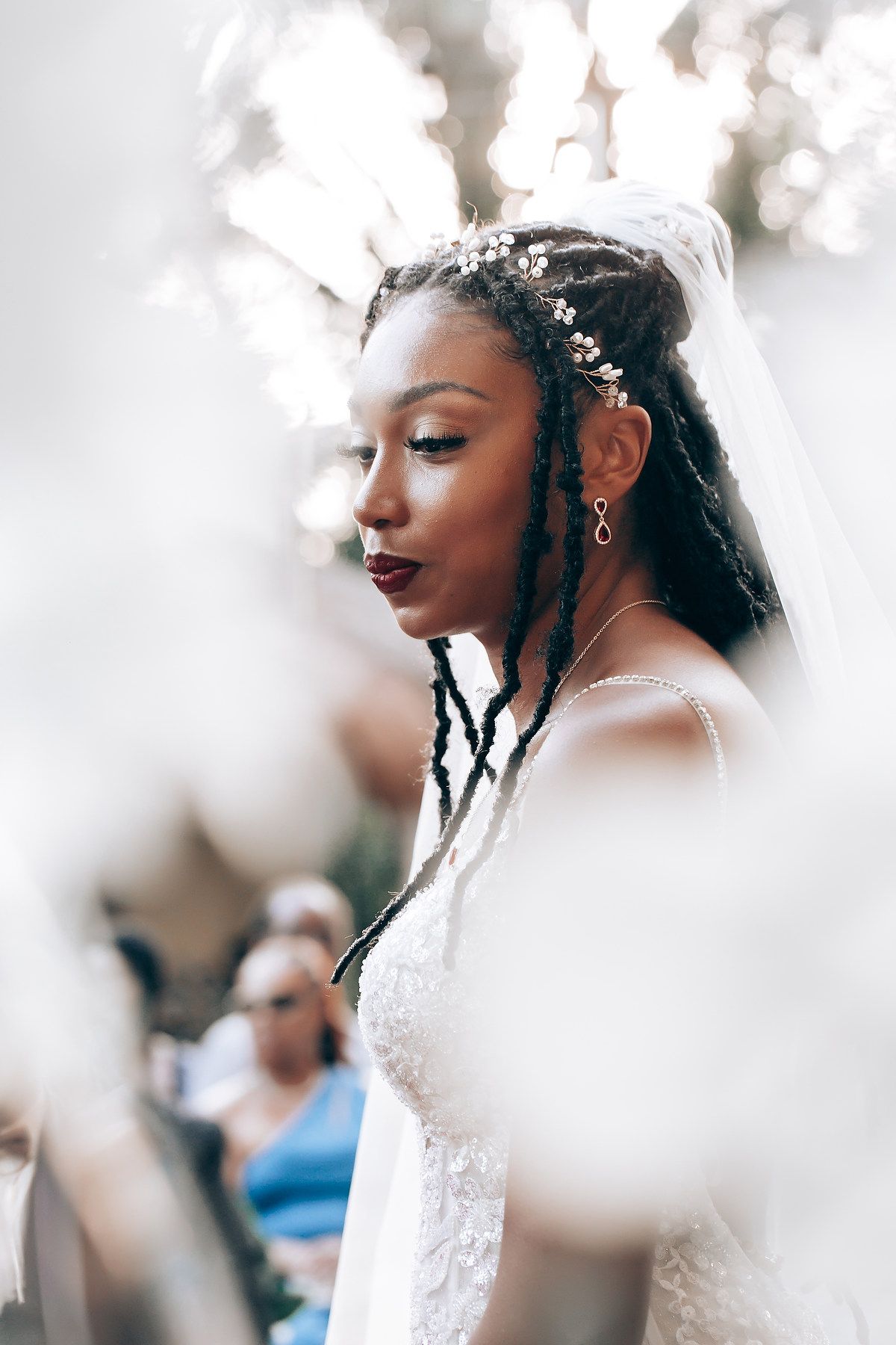 A bride in a white wedding dress with delicate floral details is photographed through a soft, dreamy focus.