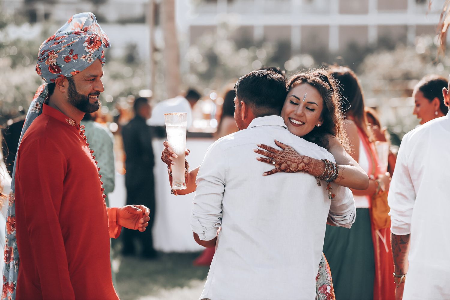 Wedding celebration scene with guests in red and white attire mingling at an outdoor venue.