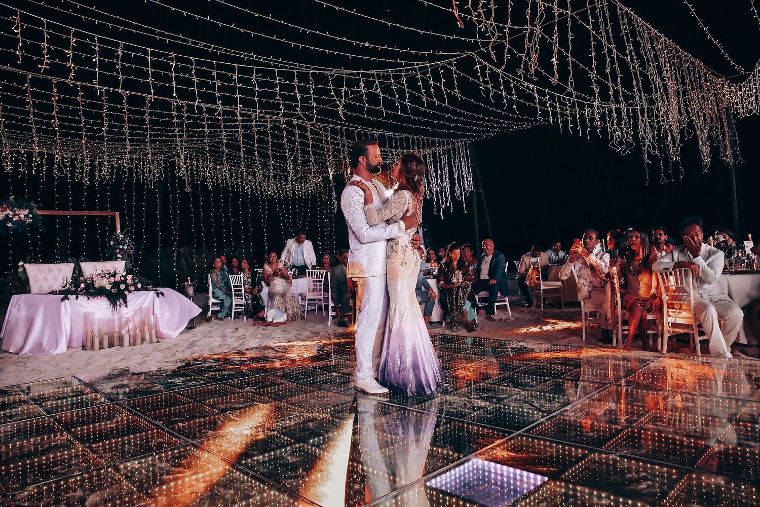 Wedding reception venue decorated with twinkling string lights and white floral arrangements creating a romantic atmosphere.