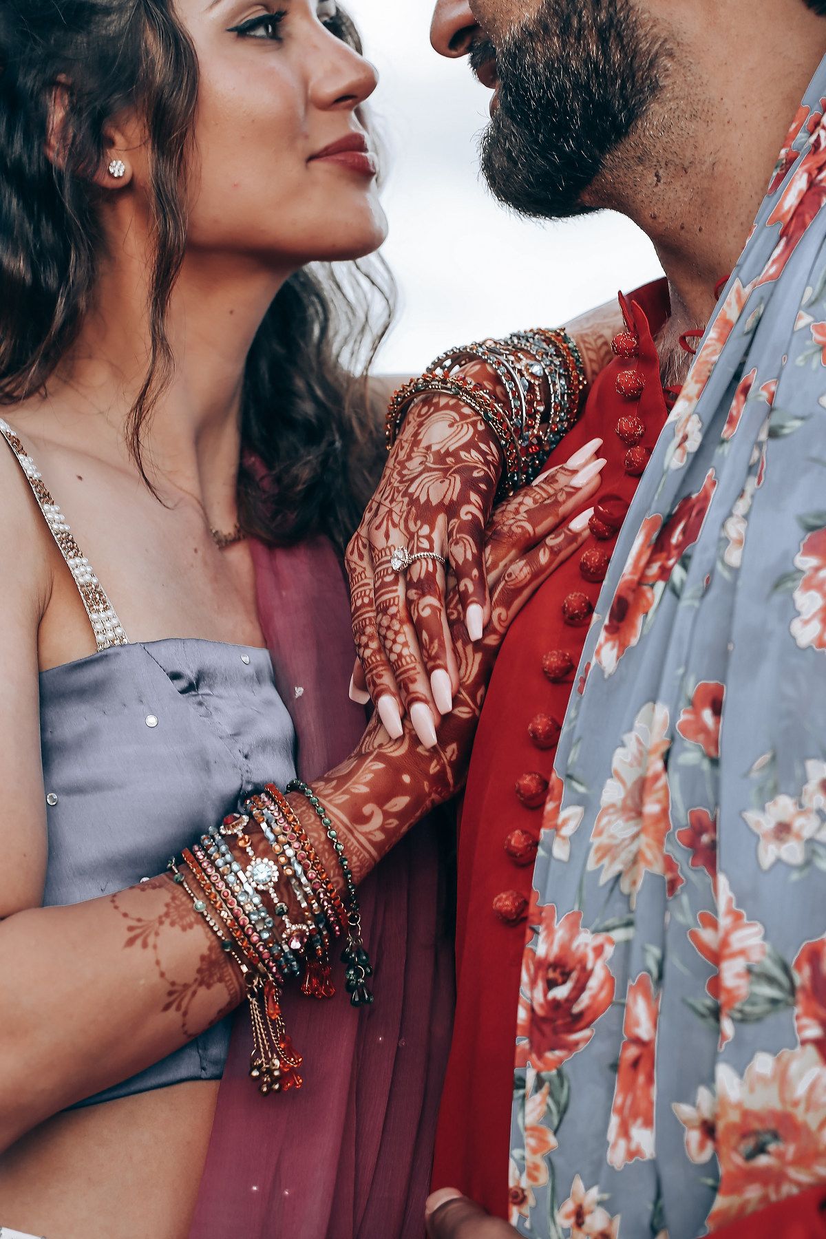 Romantic couple in traditional Indian attire with intricate henna designs and bangles embracing in intimate moment.