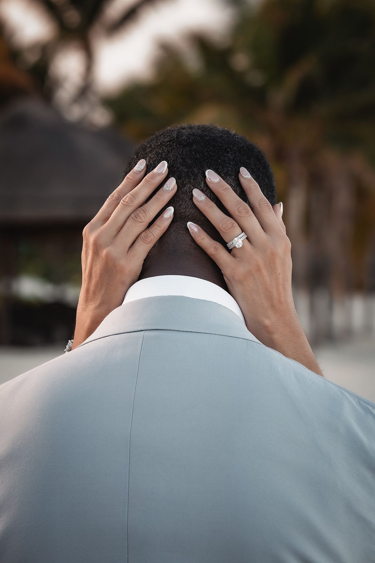 Close-up view of hands wearing an engagement ring placed on a person wearing a light gray suit.