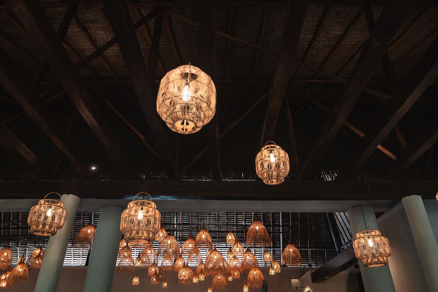 Elegant crystal chandeliers hang from a dark wooden beam ceiling at a wedding reception venue.
