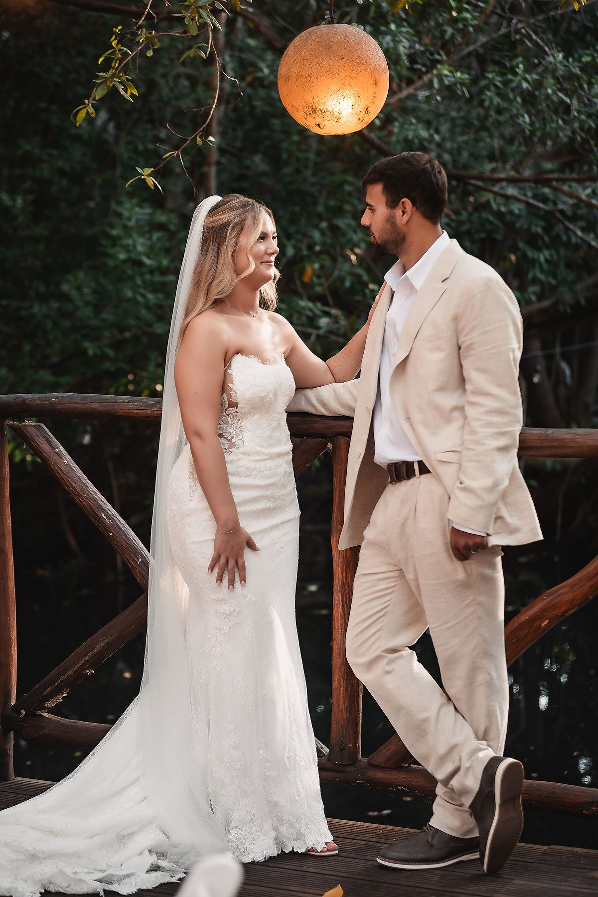 Romantic outdoor wedding moment captured under a glowing paper lantern at sunset.