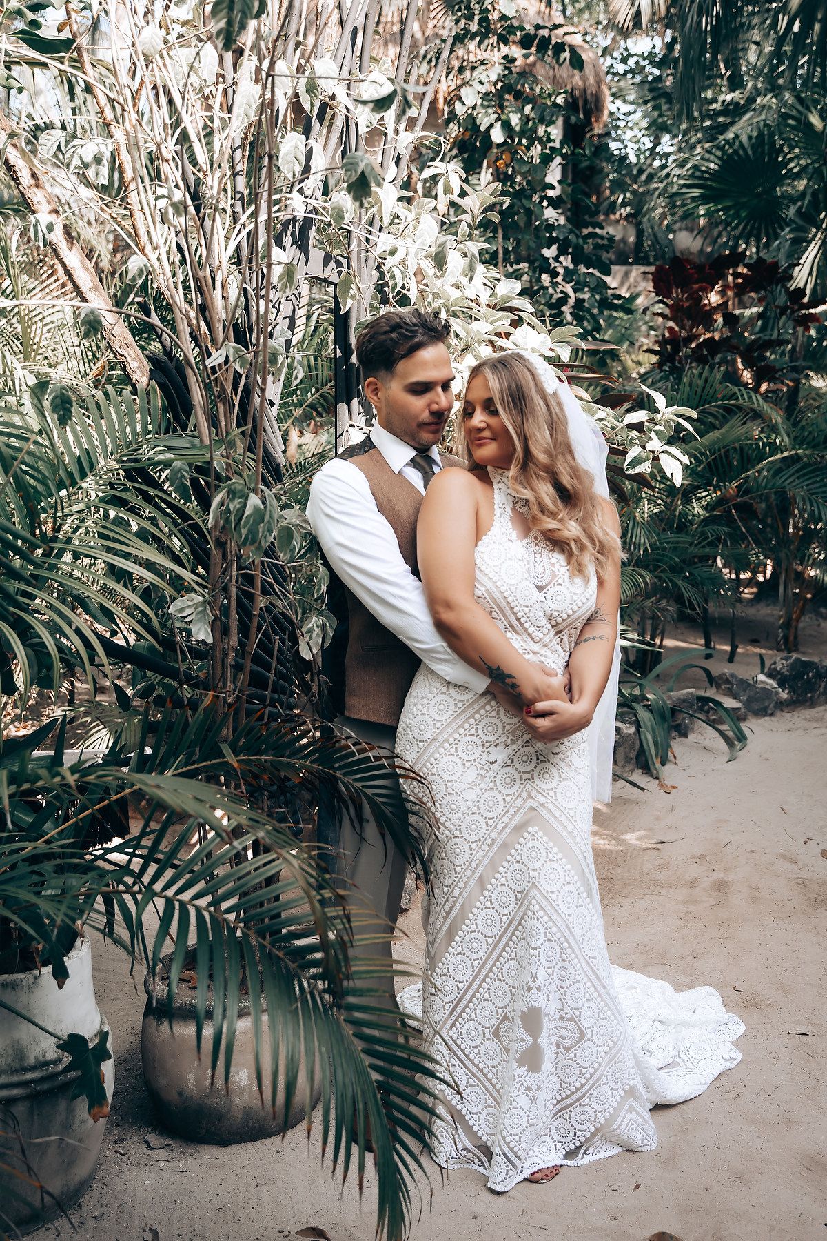 Romantic wedding couple embracing in a tropical garden setting with natural greenery.