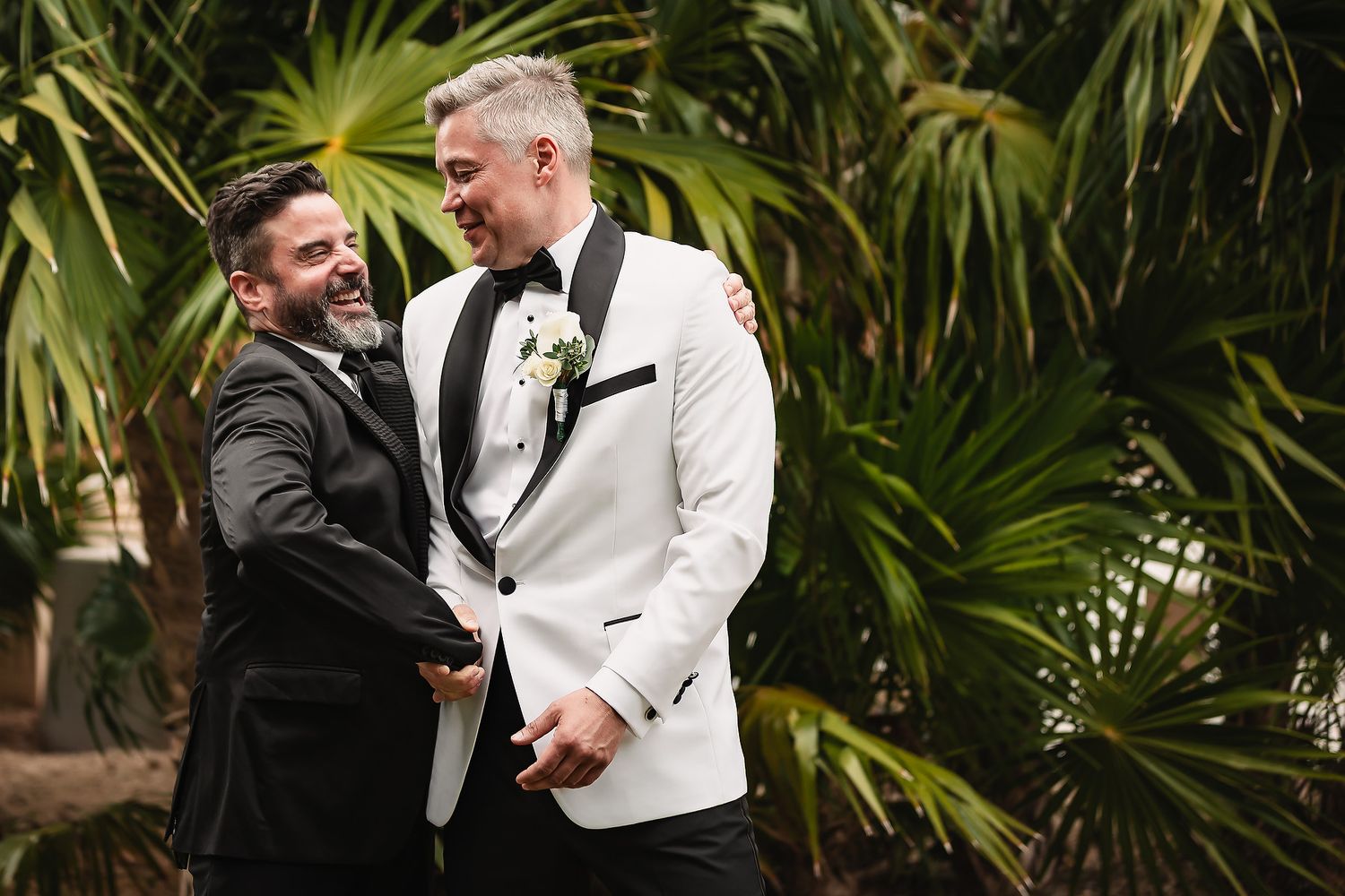 Wedding couple shares an intimate moment surrounded by lush tropical palm trees in an outdoor garden setting.