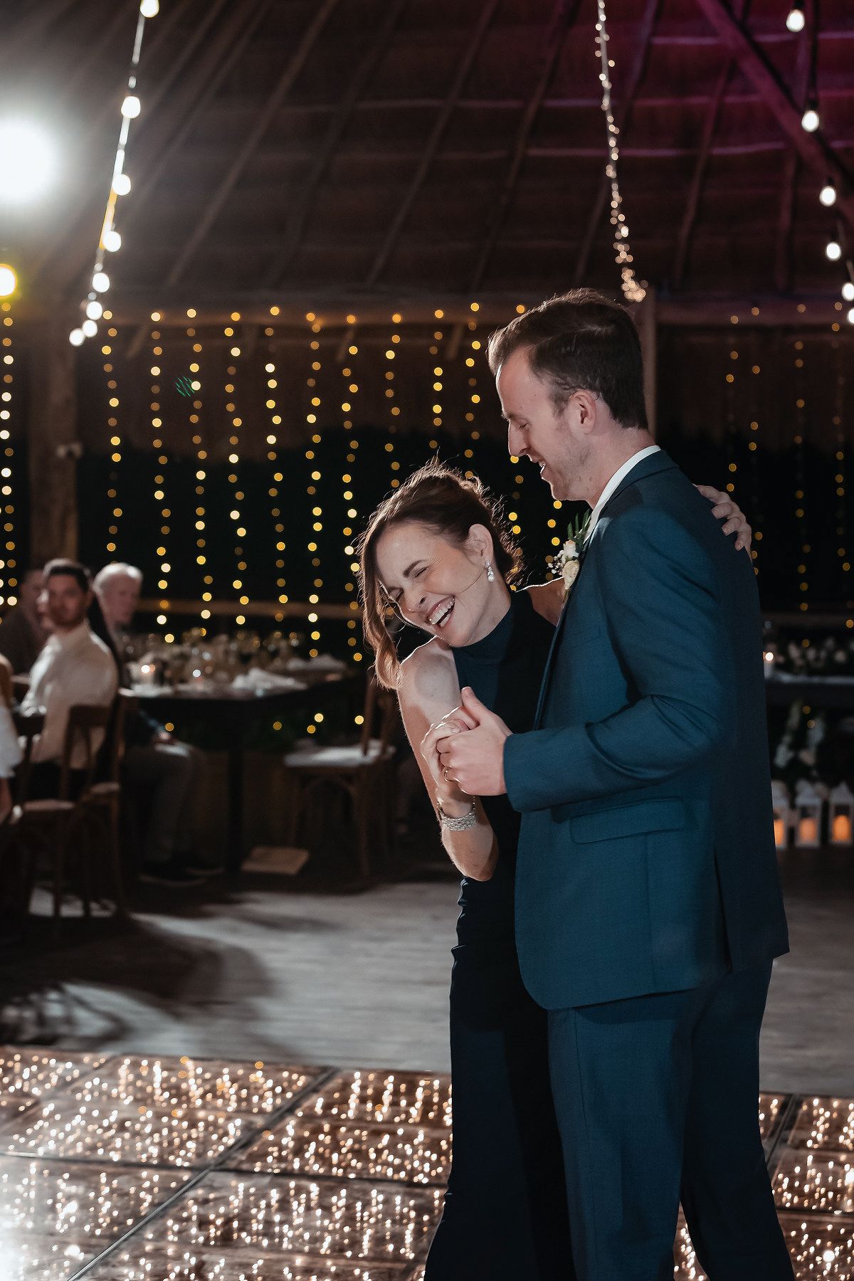 A couple shares a joyful first dance at a wedding reception adorned with warm fairy lights in a rustic venue.
