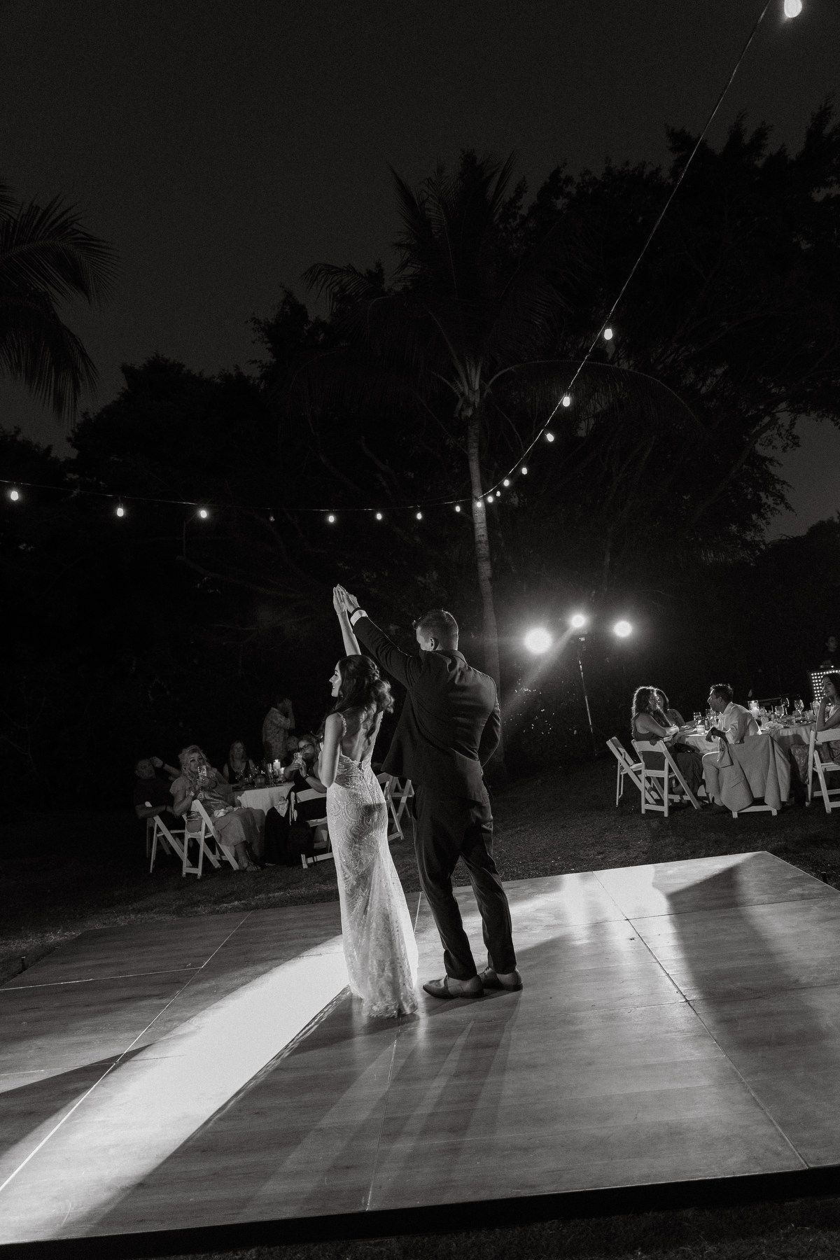 Bride and groom share their first dance on an outdoor dance floor under string lights at a nighttime wedding reception.