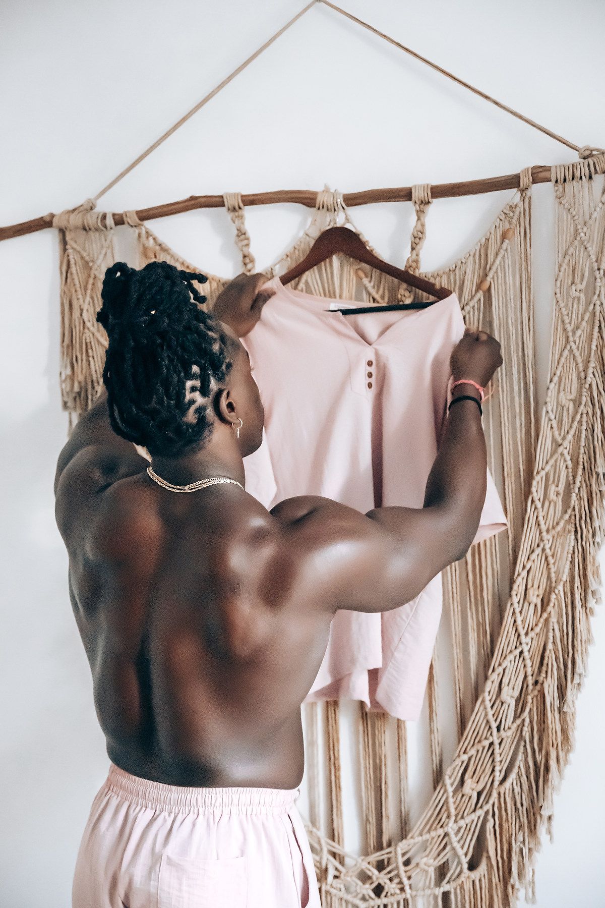 A shirtless man hanging clothes on a macrame wall hanging in a minimalist room.