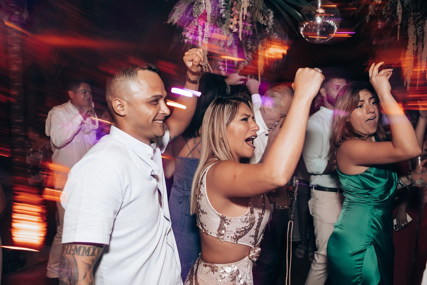 Wedding reception dance party with guests in vibrant red and green dresses under evening lighting.