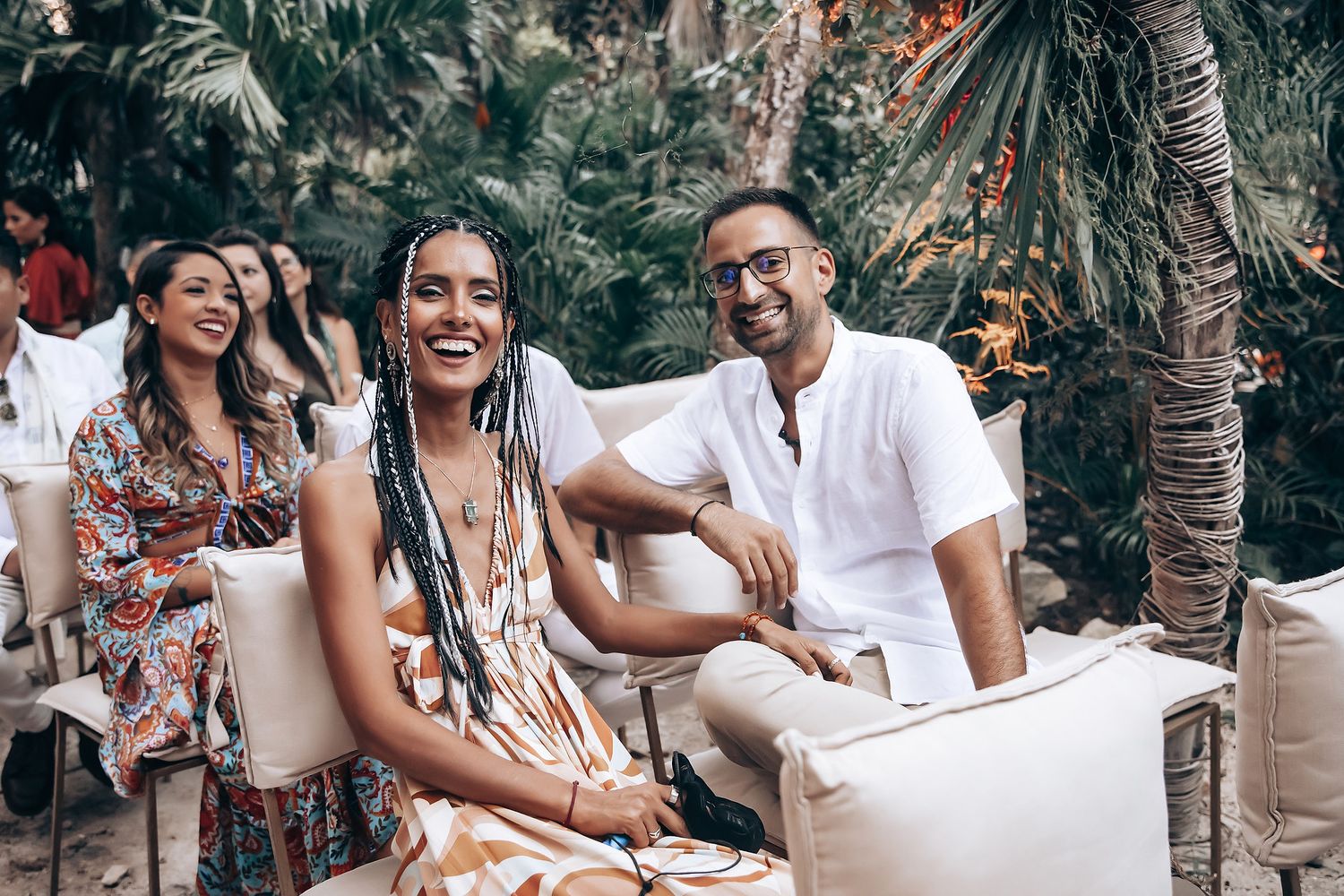 People in traditional Mexican attire socializing and laughing at an outdoor gathering with palm trees.