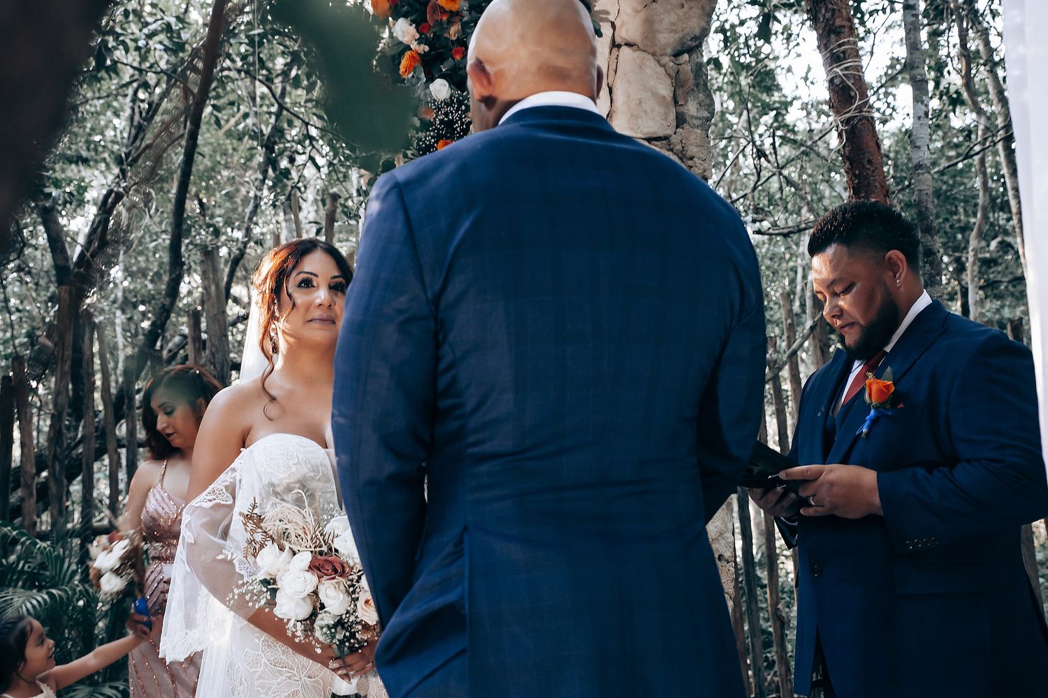 A wedding ceremony takes place in a serene forest setting with guests gathered around.