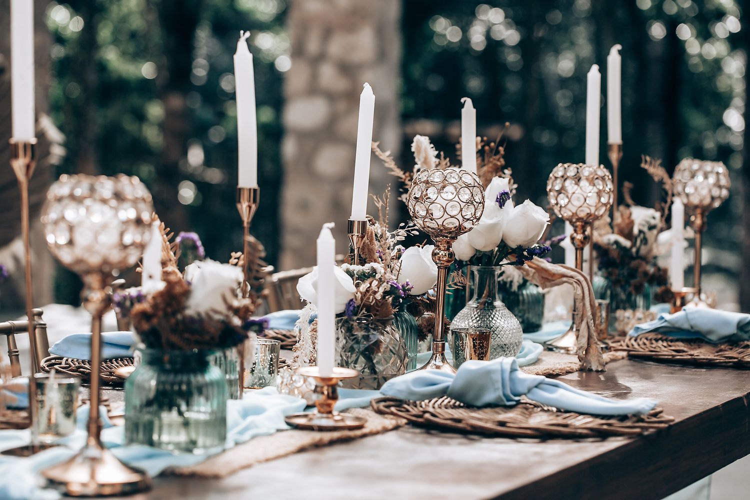 Elegant wedding reception table setting with white flowers and candles in a rustic outdoor venue.