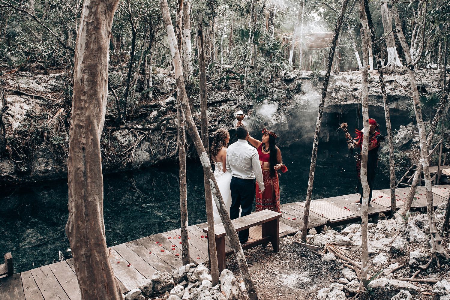 A series of wooden walkways and bridges wind through a lush forest landscape near a rocky cliff face.