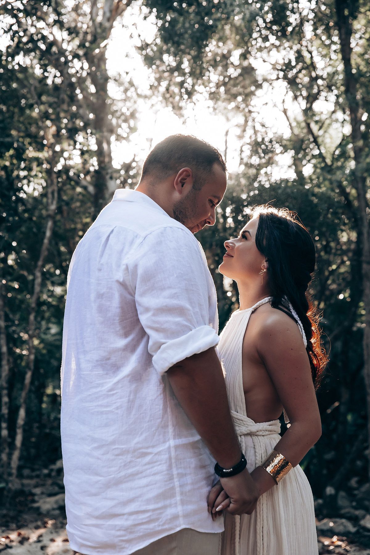 Romantic embrace in white clothing surrounded by sunlit forest scenery.