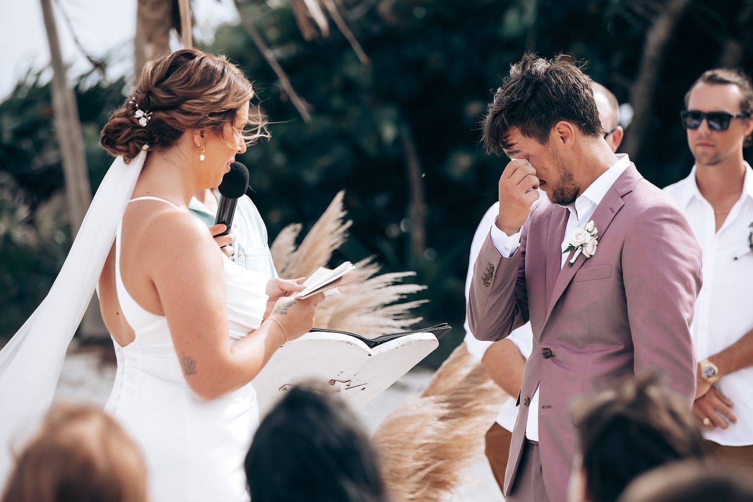 Wedding guests celebrate on a tropical beach with palm trees swaying in the background.