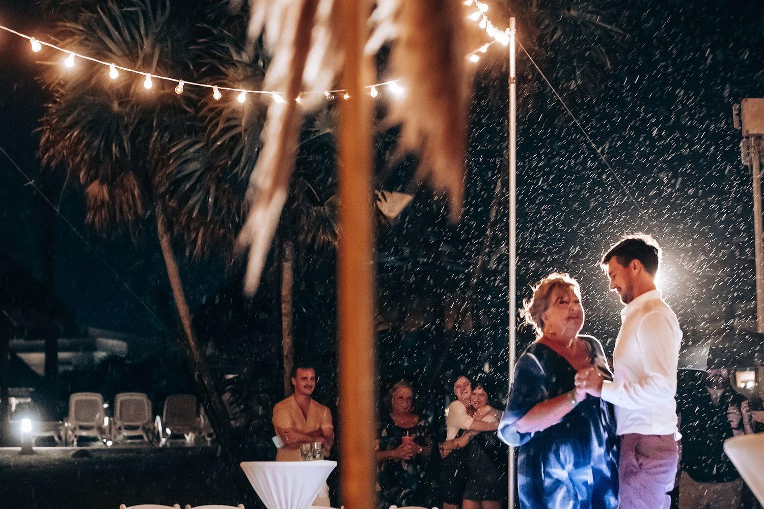 Couples dance under twinkling lights at a romantic beach wedding reception.