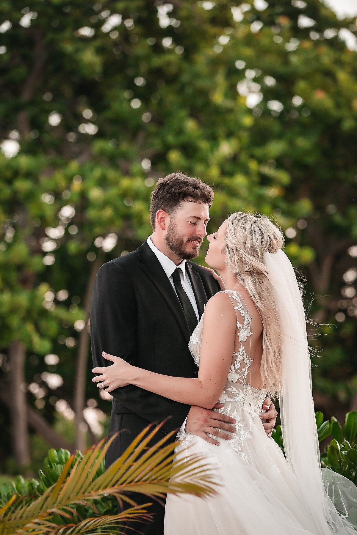 A couple shares a romantic moment among tropical palm fronds in an outdoor garden setting.
