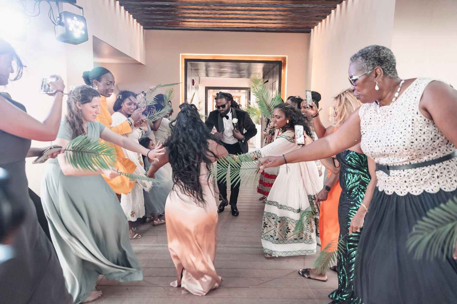 Joyful wedding guests dancing and celebrating as the groom walks through a festive cultural ceremony.