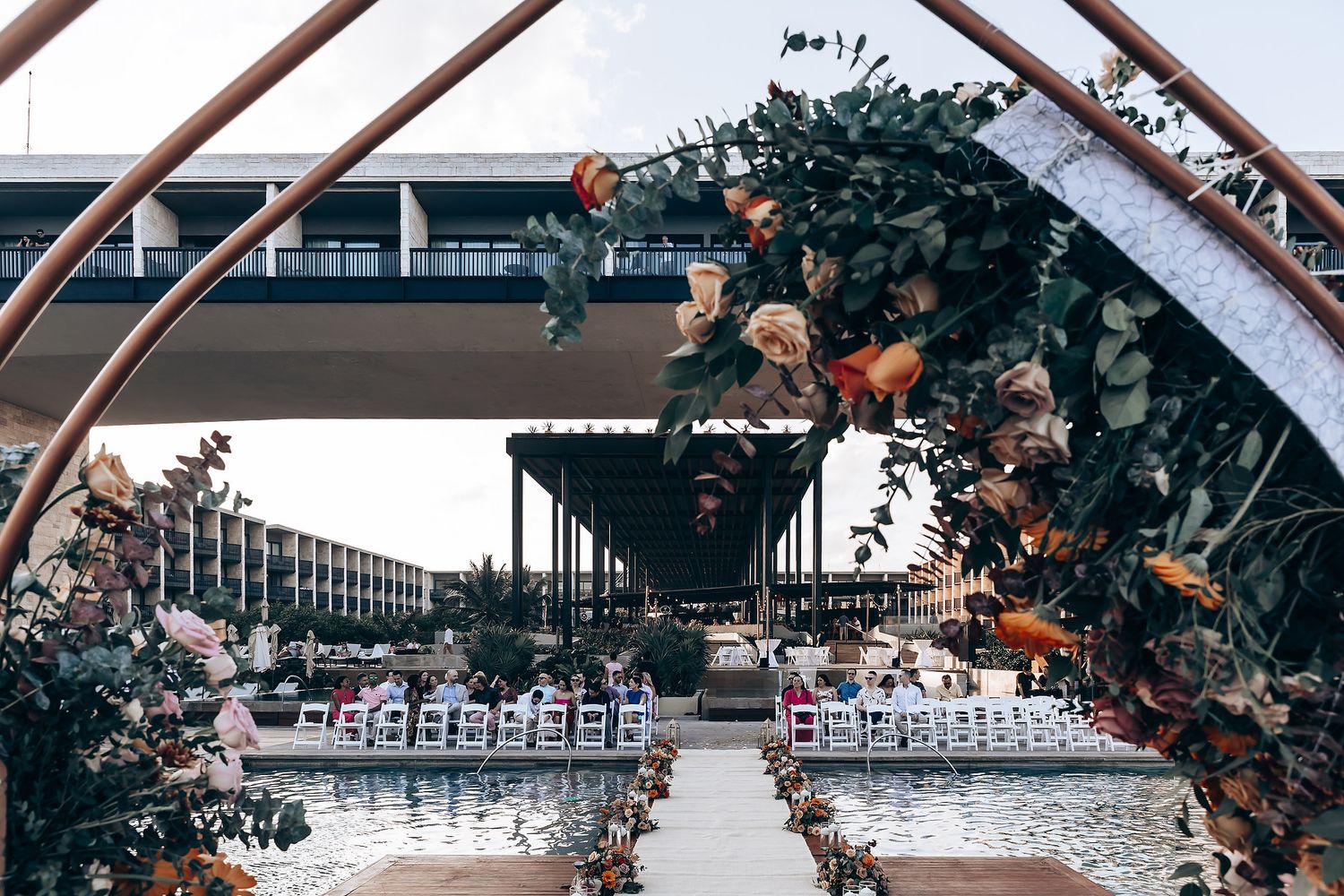Wedding ceremony setup with wooden arch and floral arrangements against a waterfront backdrop.