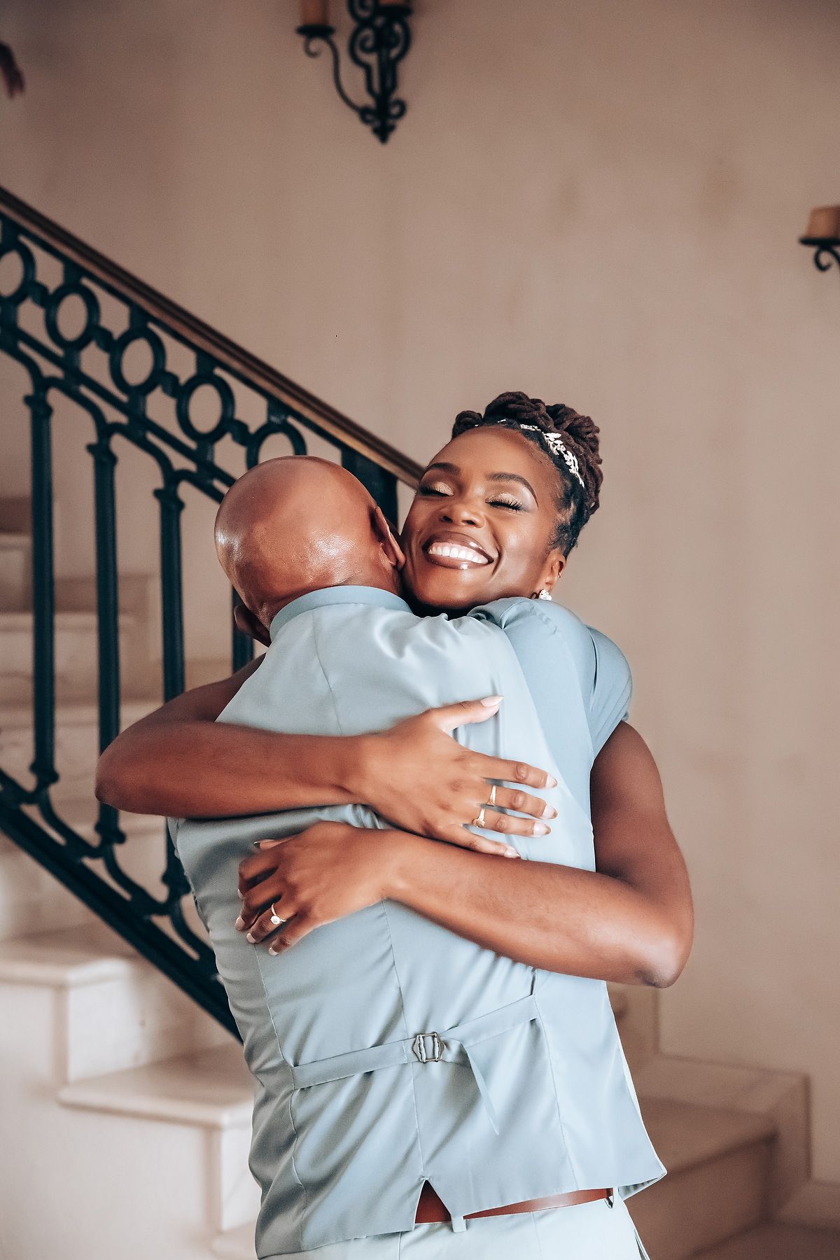 Joyful embrace shared on elegant staircase with ornate railing.