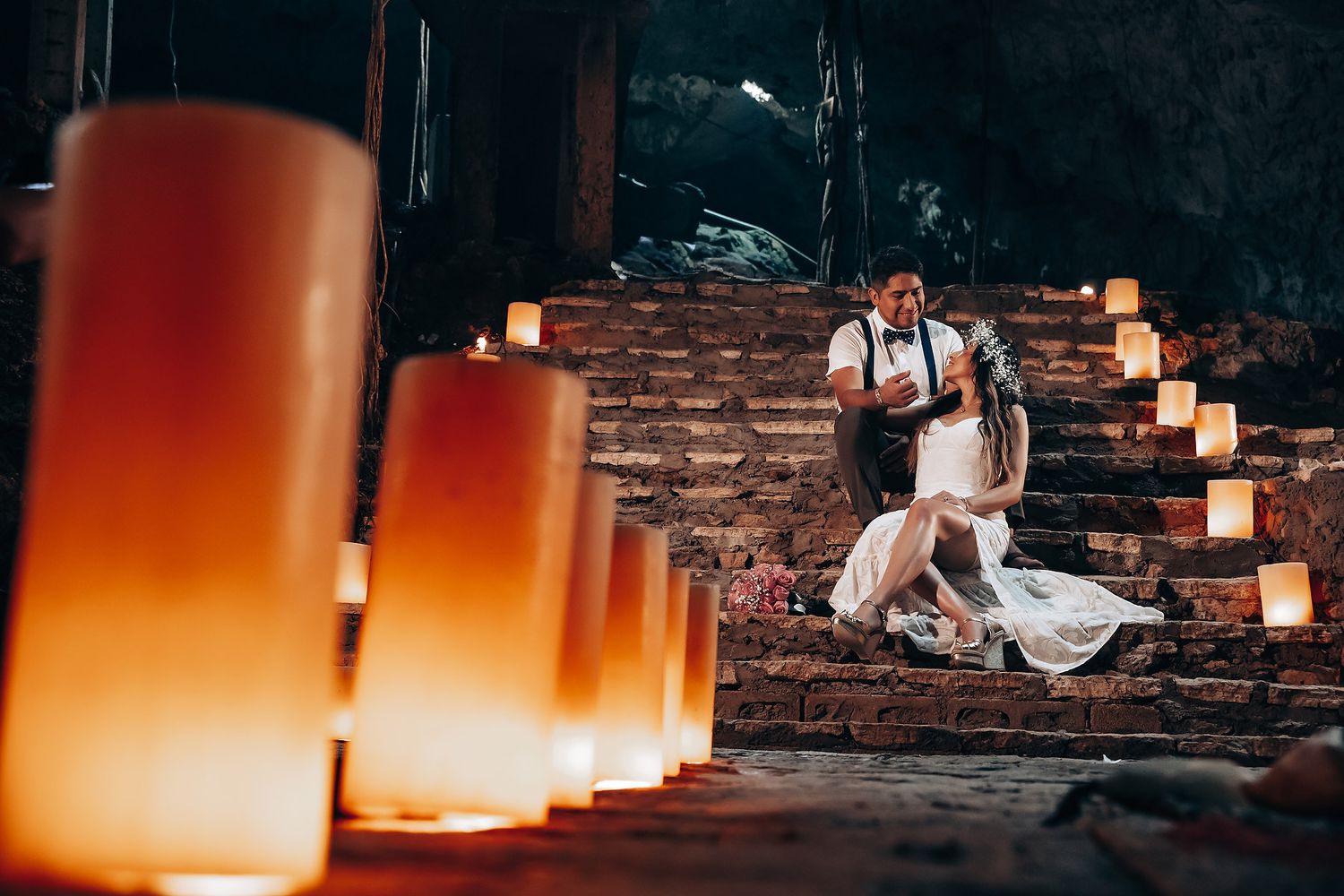 A romantic couple sits on stone steps illuminated by glowing orange lanterns creating an intimate atmosphere at night.