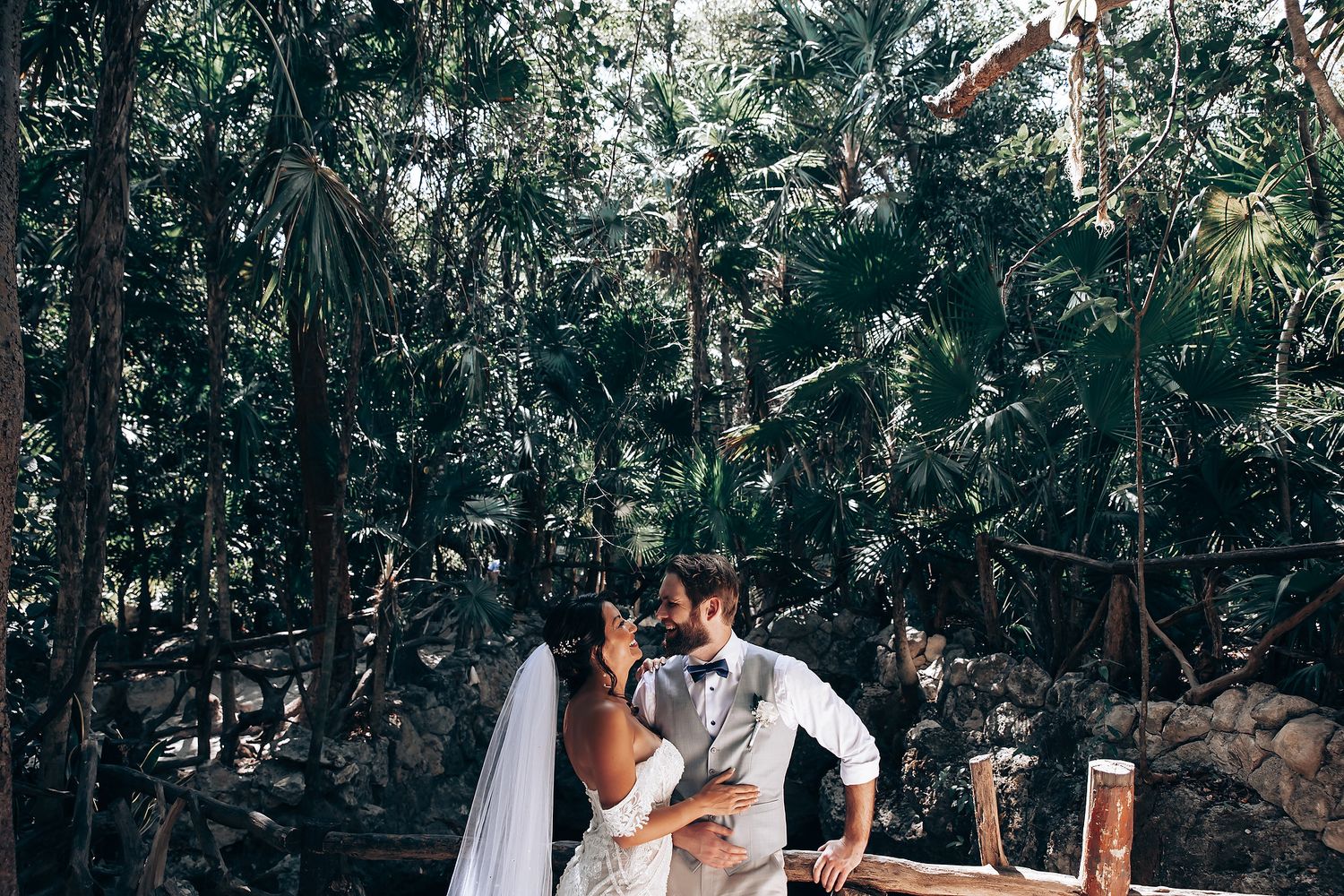 Couple shares intimate moment during outdoor wedding ceremony surrounded by lush tropical foliage.