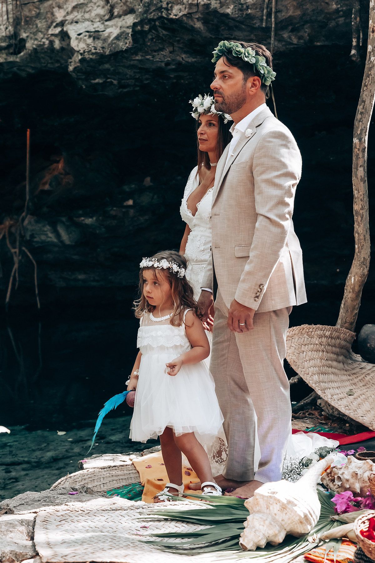 A wedding couple in light beige and white attire pose together on a beach setting with tropical decor.