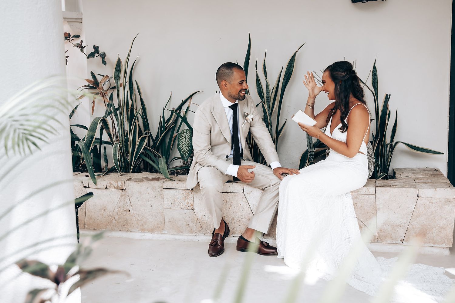 A romantic wedding photoshoot featuring intimate poses against a white interior with tropical plants.