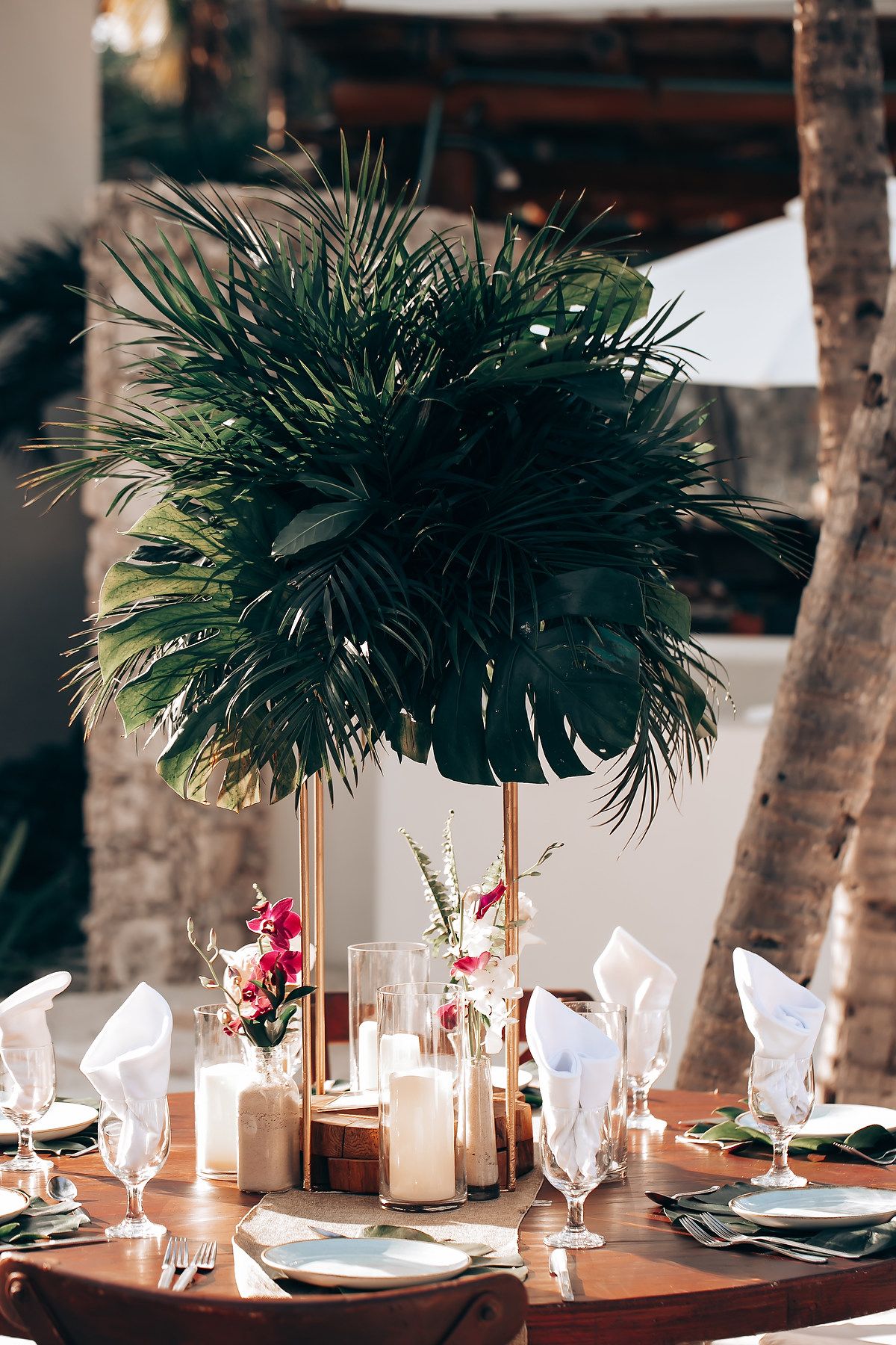Elegant wedding reception table setting with palm leaf centerpieces and white napkins.