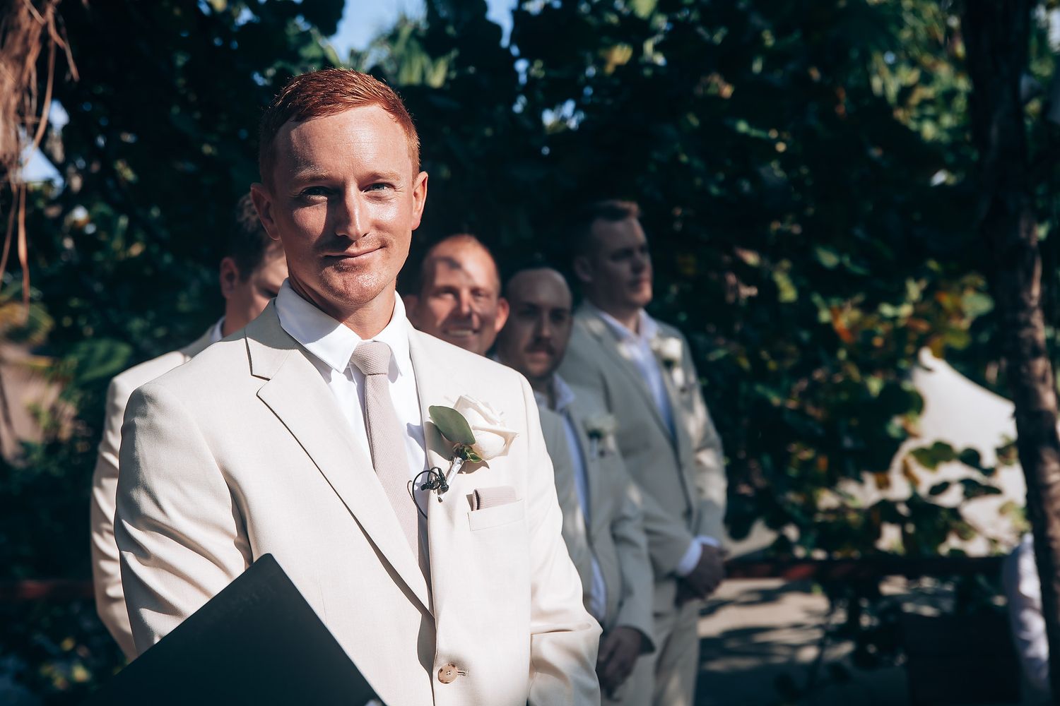 Wedding party members in white and gray attire pose for photos in a garden setting.