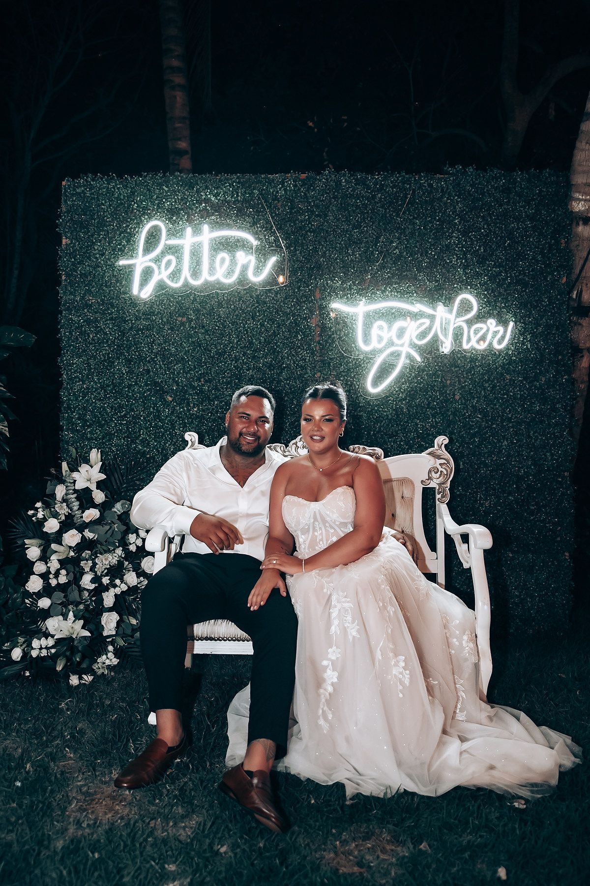 A couple sits beneath glowing neon signs during their wedding celebration.
