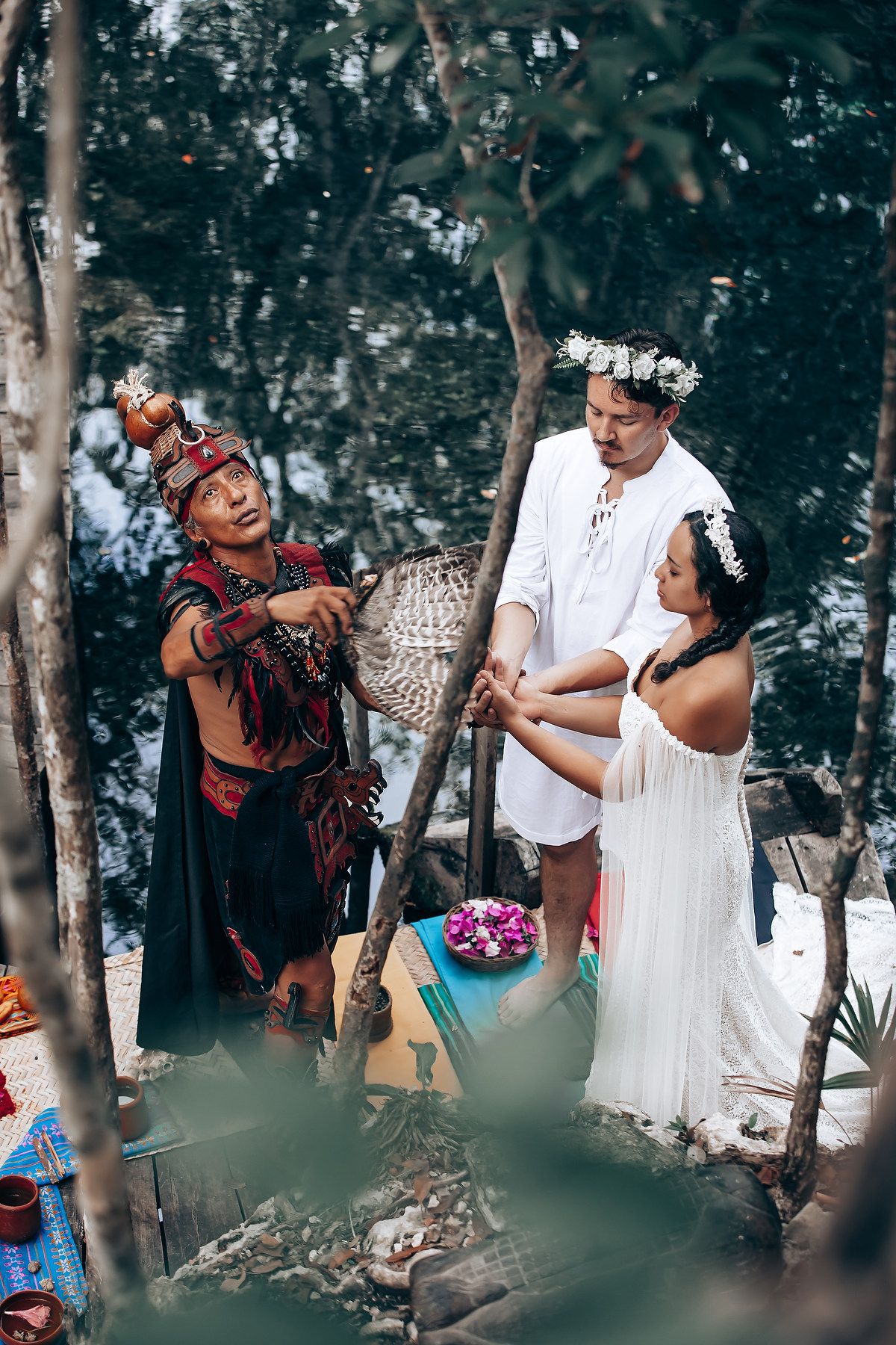 Traditional Mayan ceremony takes place in a wooded area with participants wearing white dresses and ceremonial attire.