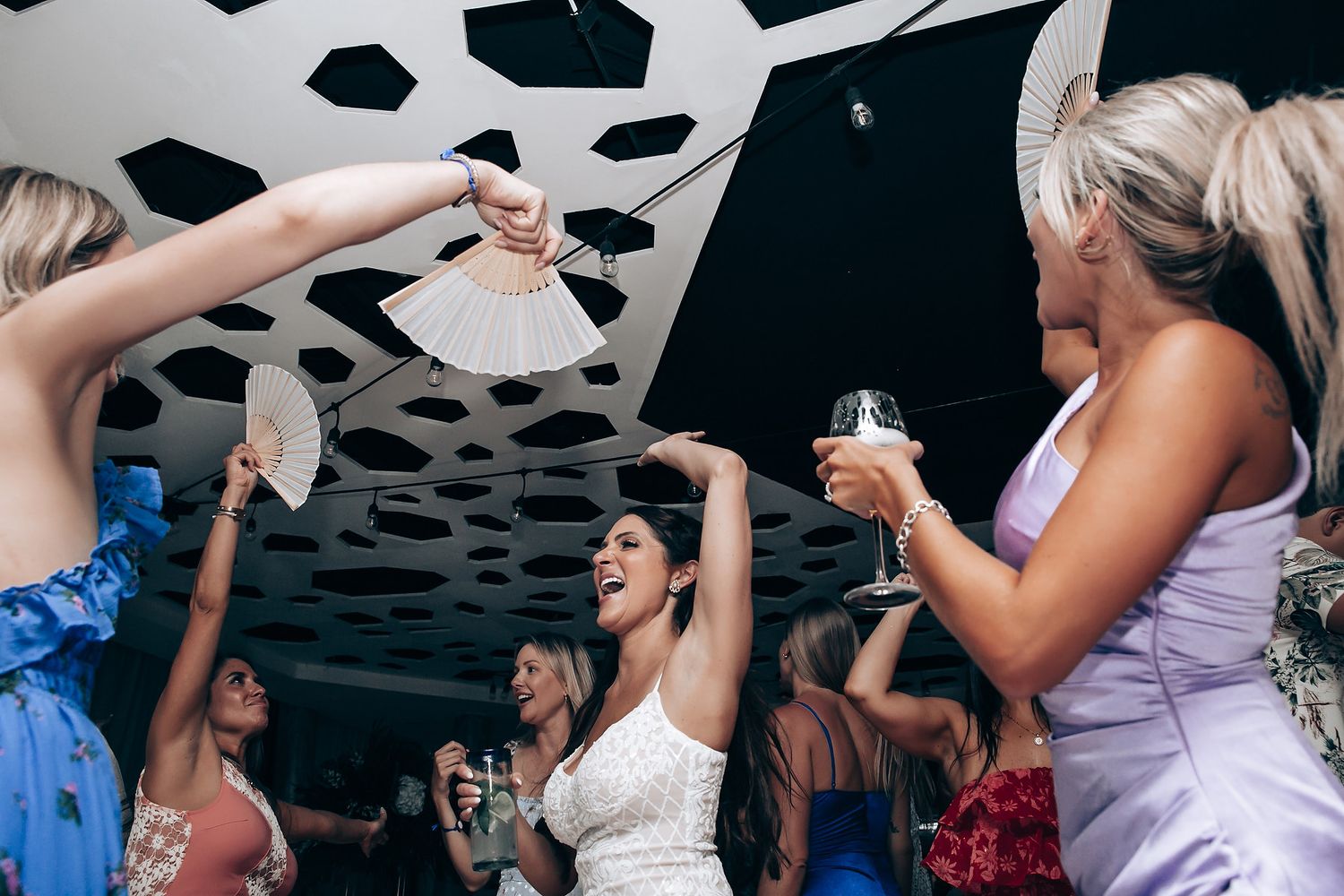 Wedding celebration with guests raising champagne glasses under modern spotted ceiling design.