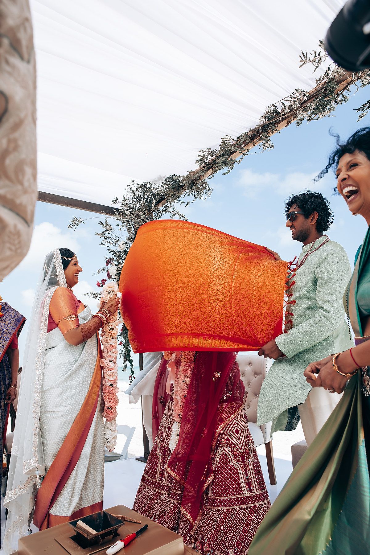 Outdoor wedding ceremony under a decorated arch with guests in traditional Indian attire.