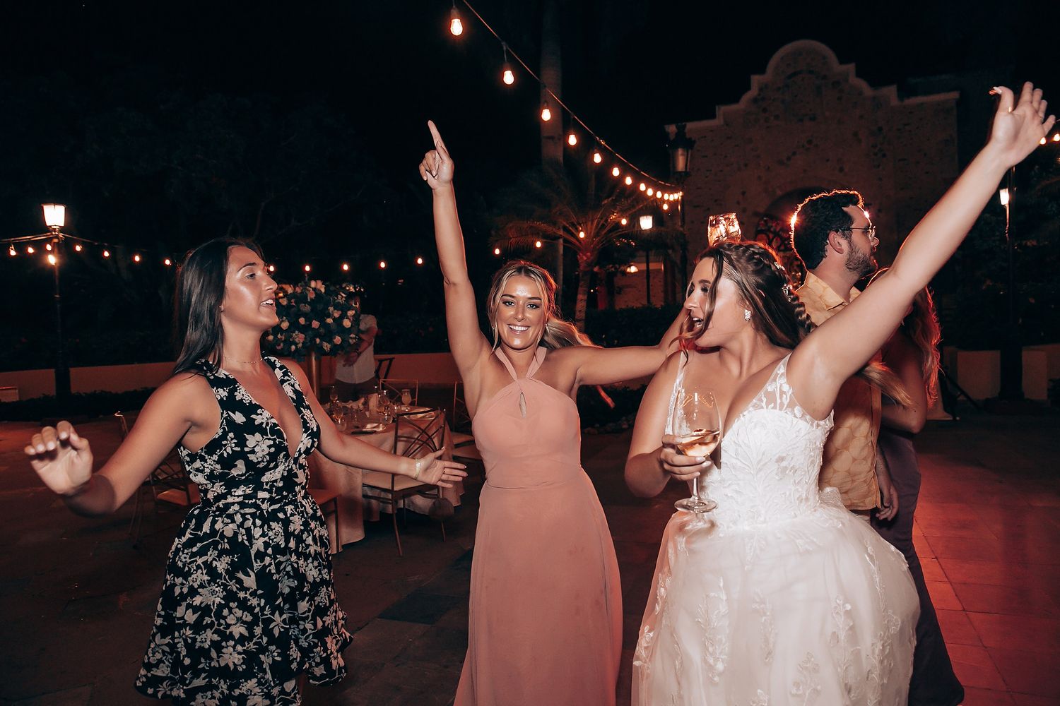 Wedding guests dance and celebrate on an outdoor dance floor illuminated by overhead string lights.