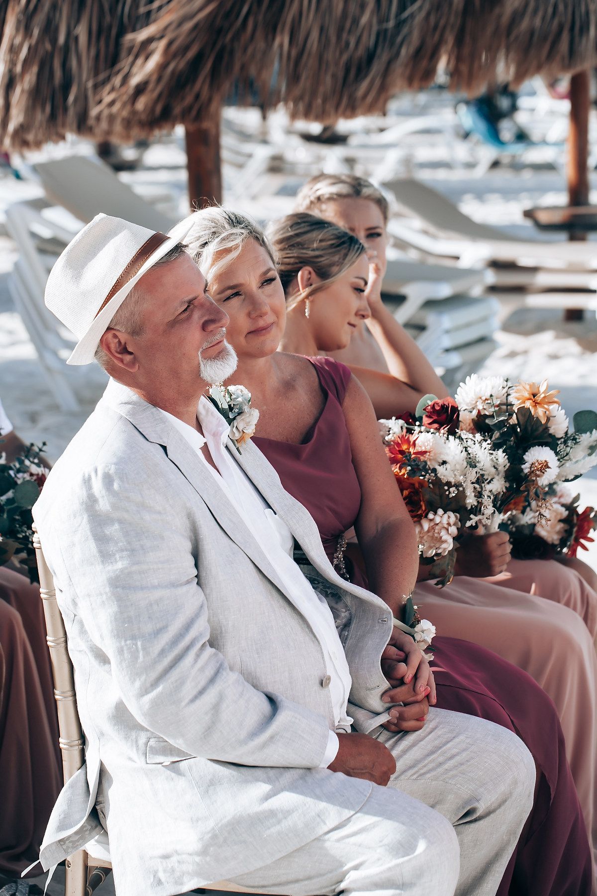 Wedding attendees seated in formal attire with floral bouquets at beachside ceremony.