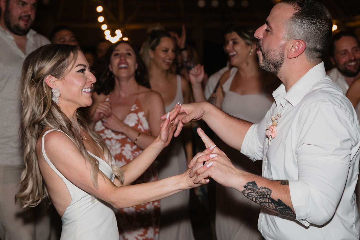 Bride and groom hold hands and smile during their first dance at evening wedding reception.