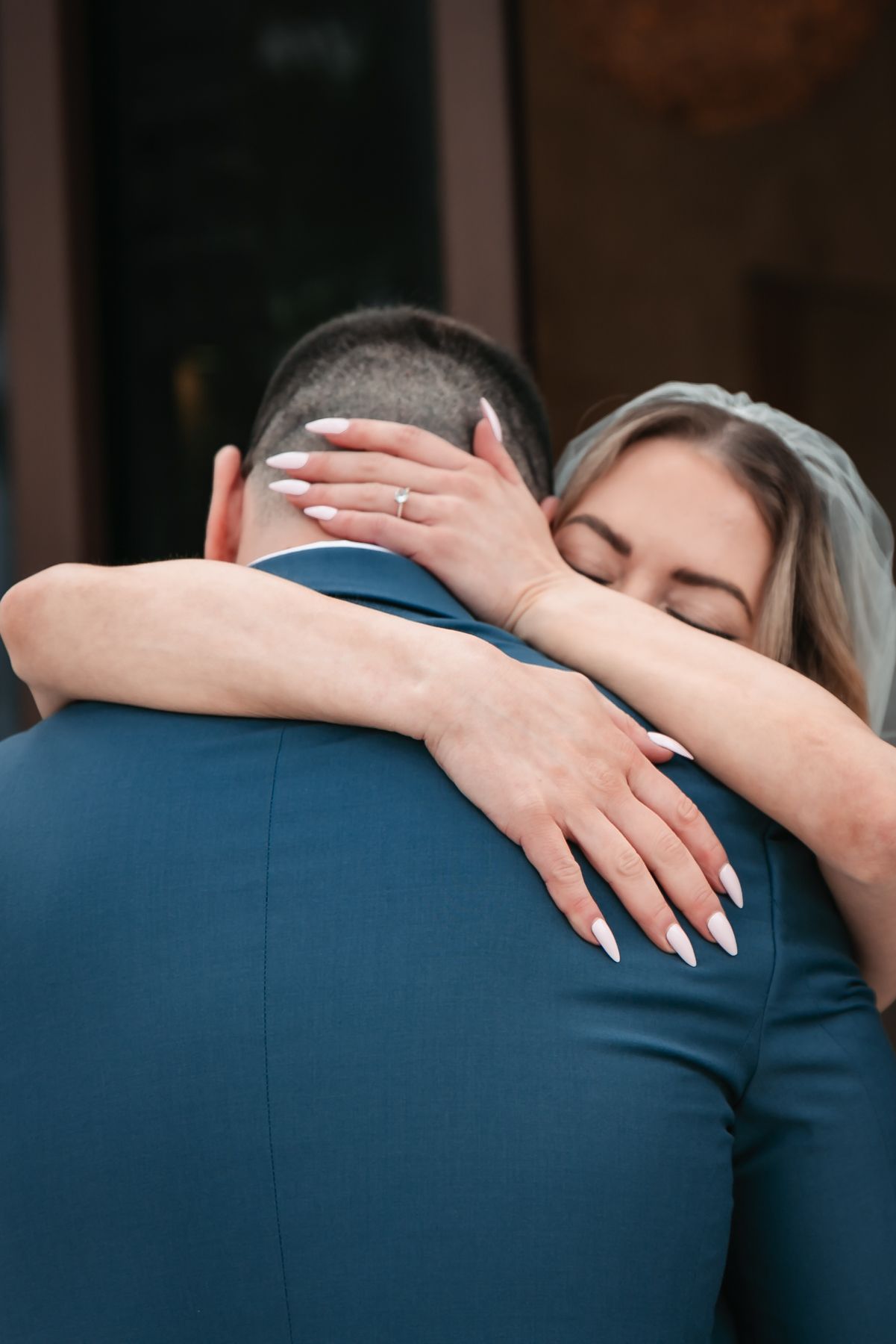 Bride with white manicure and gold ring embracing groom in blue suit during wedding ceremony.