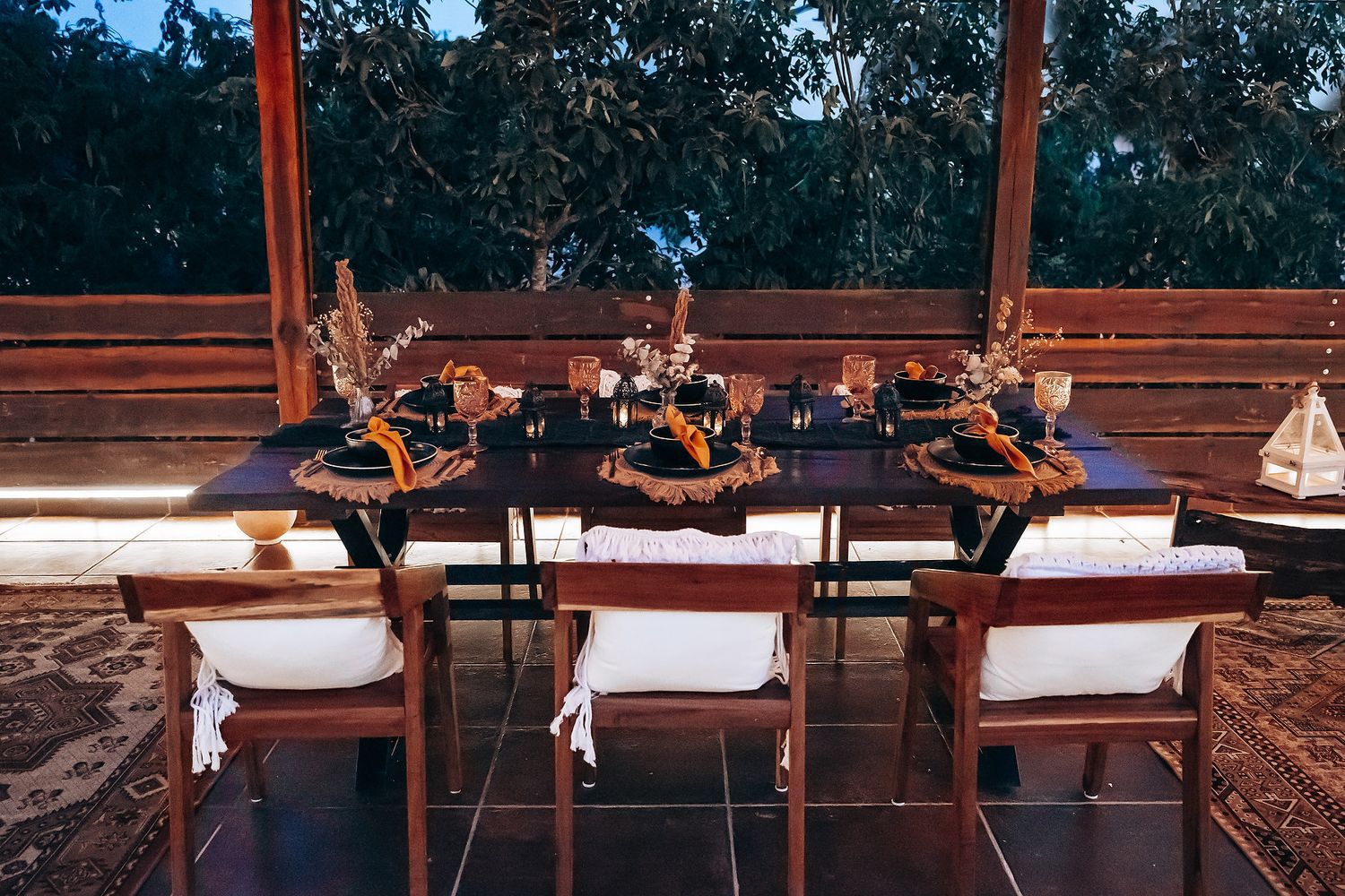 Intimate outdoor evening dinner table with dark navy linens, dried floral centerpieces, and warm string lights.