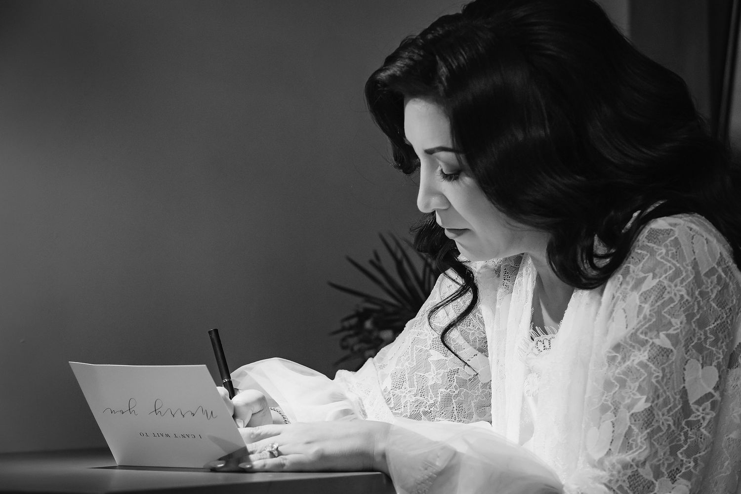 Bride writing wedding vows in black and white photo, wearing lace robe.