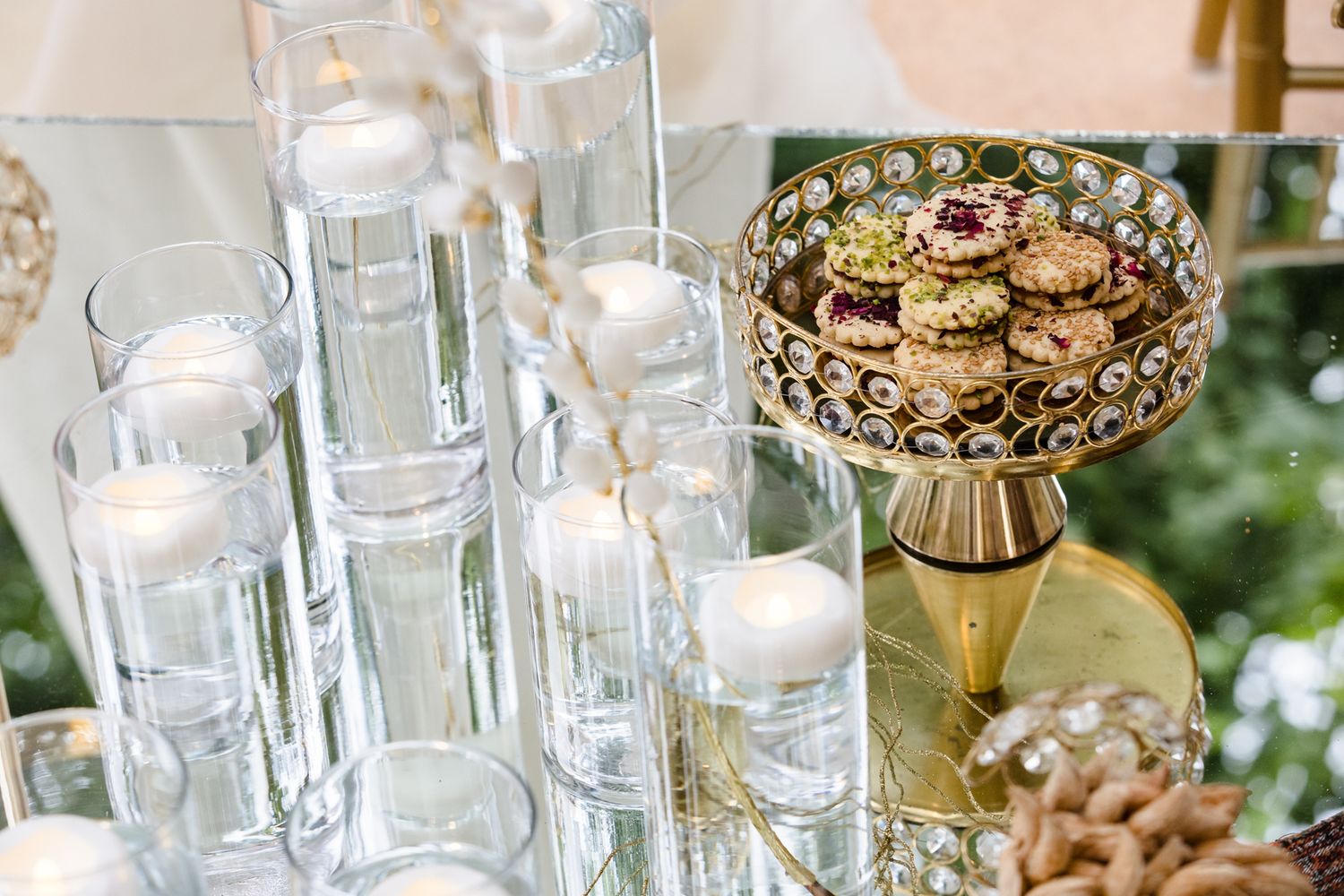 Elegant wedding dessert table with floating candle vases, crystal cylinders, and macarons on a gold ornate cake stand.