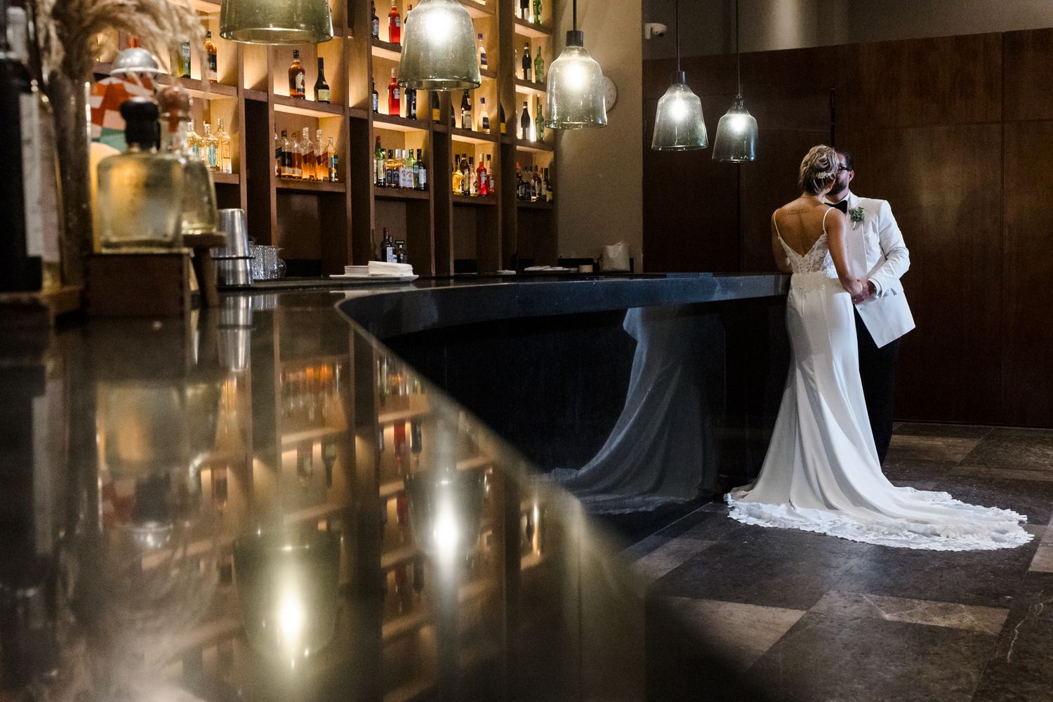 Bride and groom share an intimate moment at a luxurious bar venue, with the brides train elegantly spread.